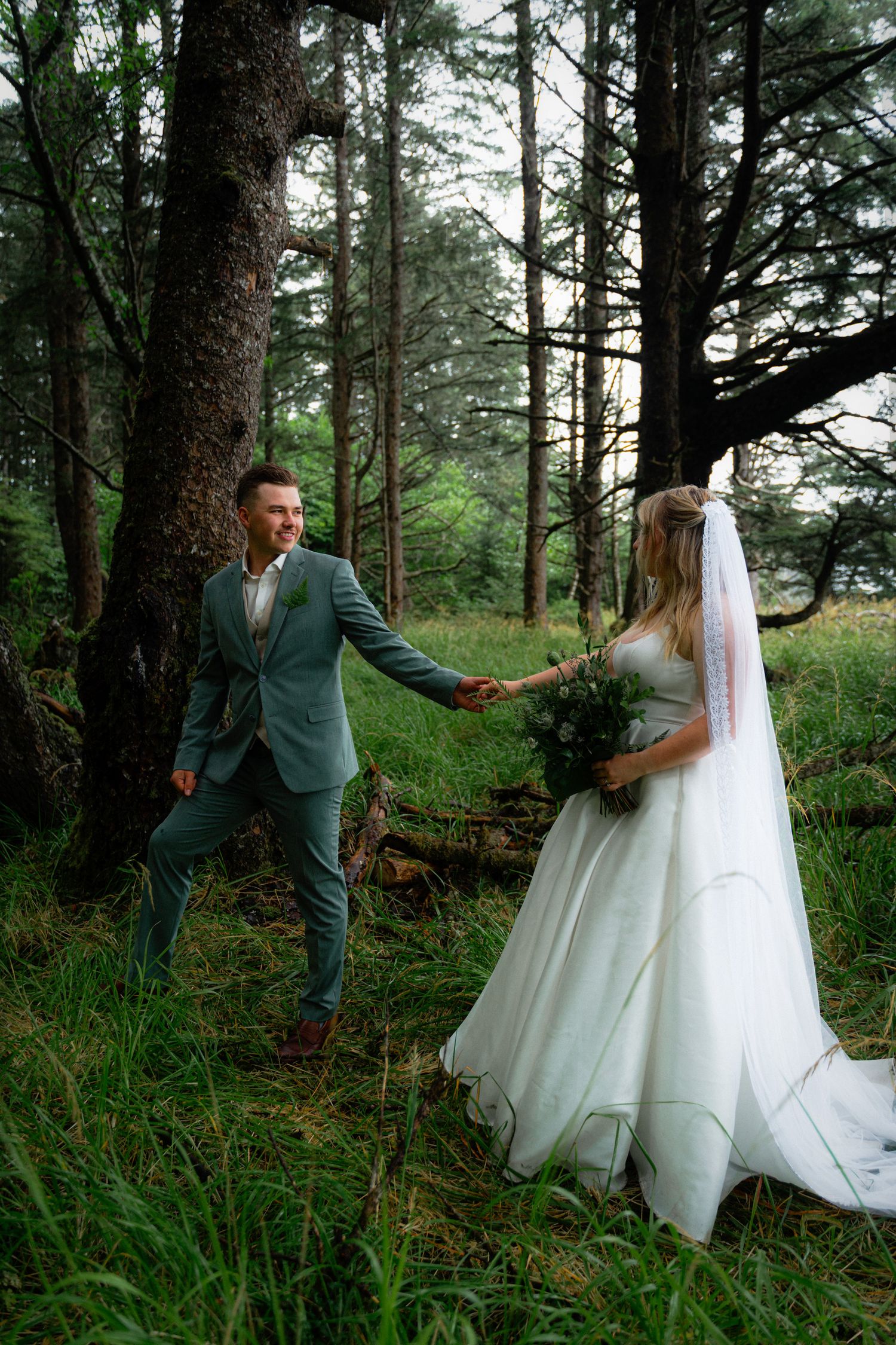 Bride and groom holding hands in lush forest setting.
