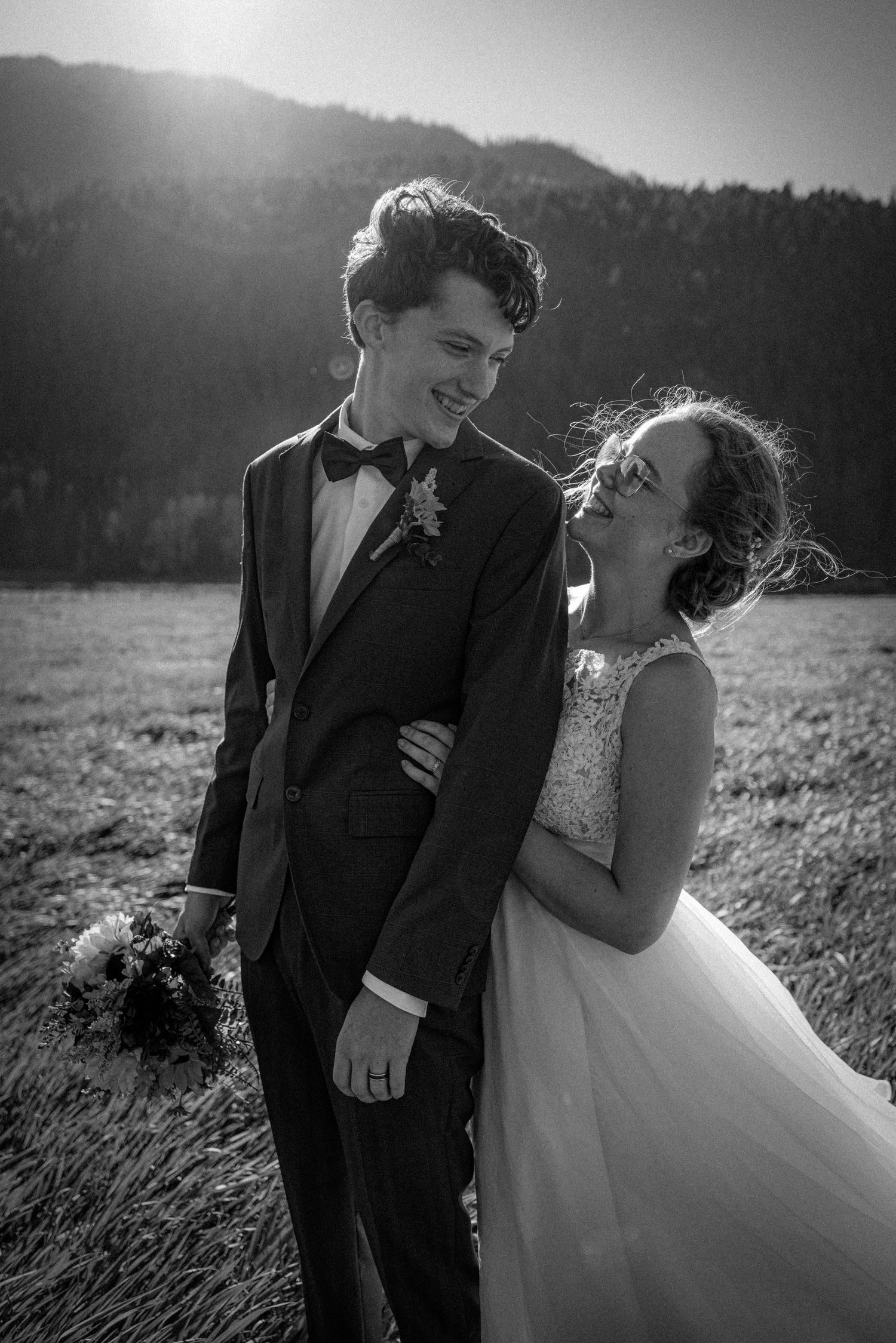 Black and white photo of laughing bride and groom in mountain meadow on wedding day.