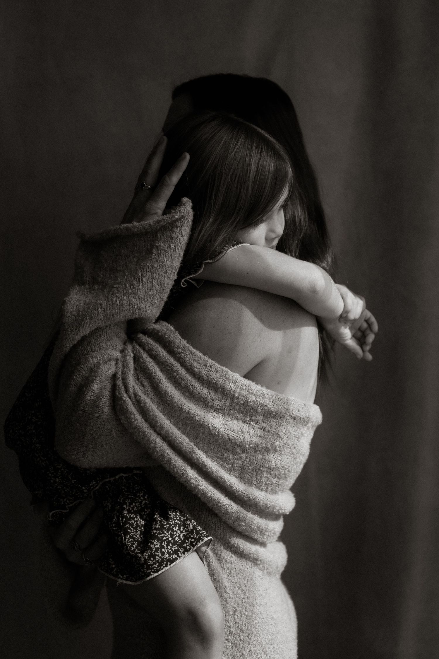 Mother embracing her little girl tightly in the window light. Studio shot