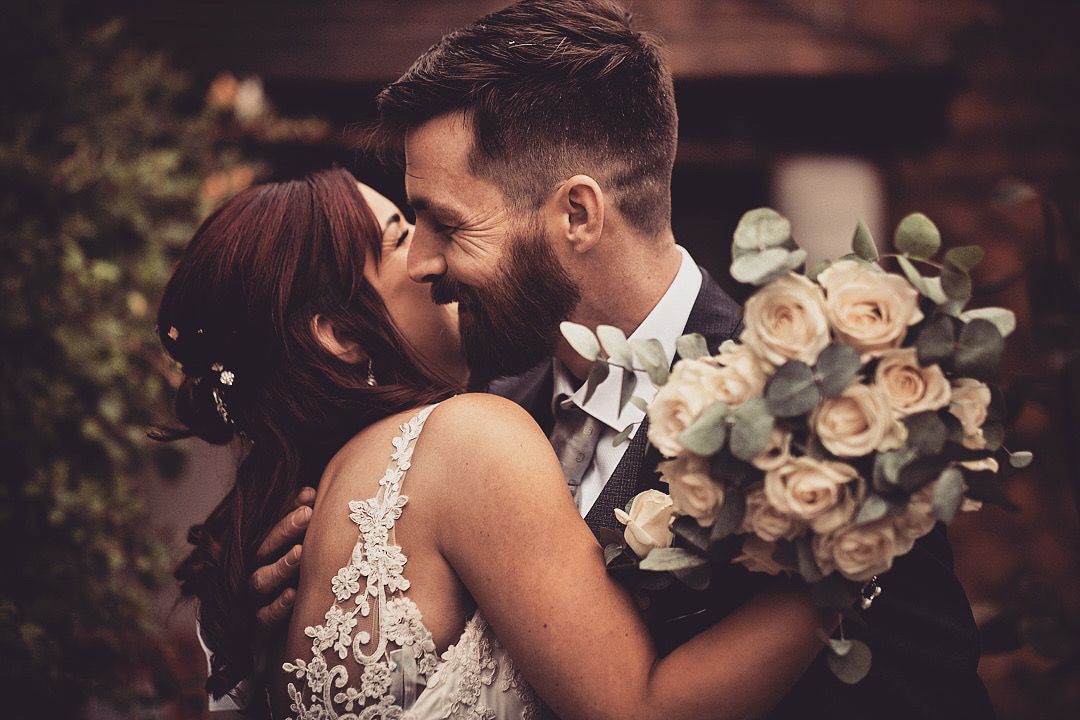 Romantic wedding couple shares intimate moments in garden setting with white floral bouquets.
