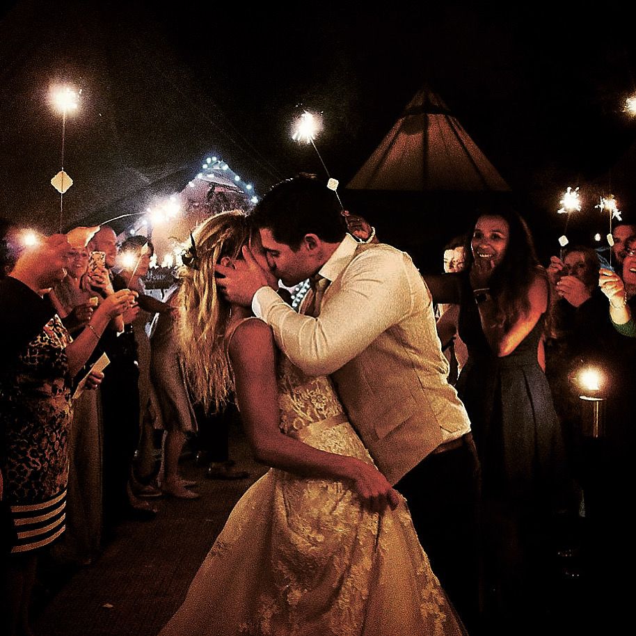 A romantic sparkler-lit nighttime wedding dance with the couple embracing in a golden gown and suit among guests.