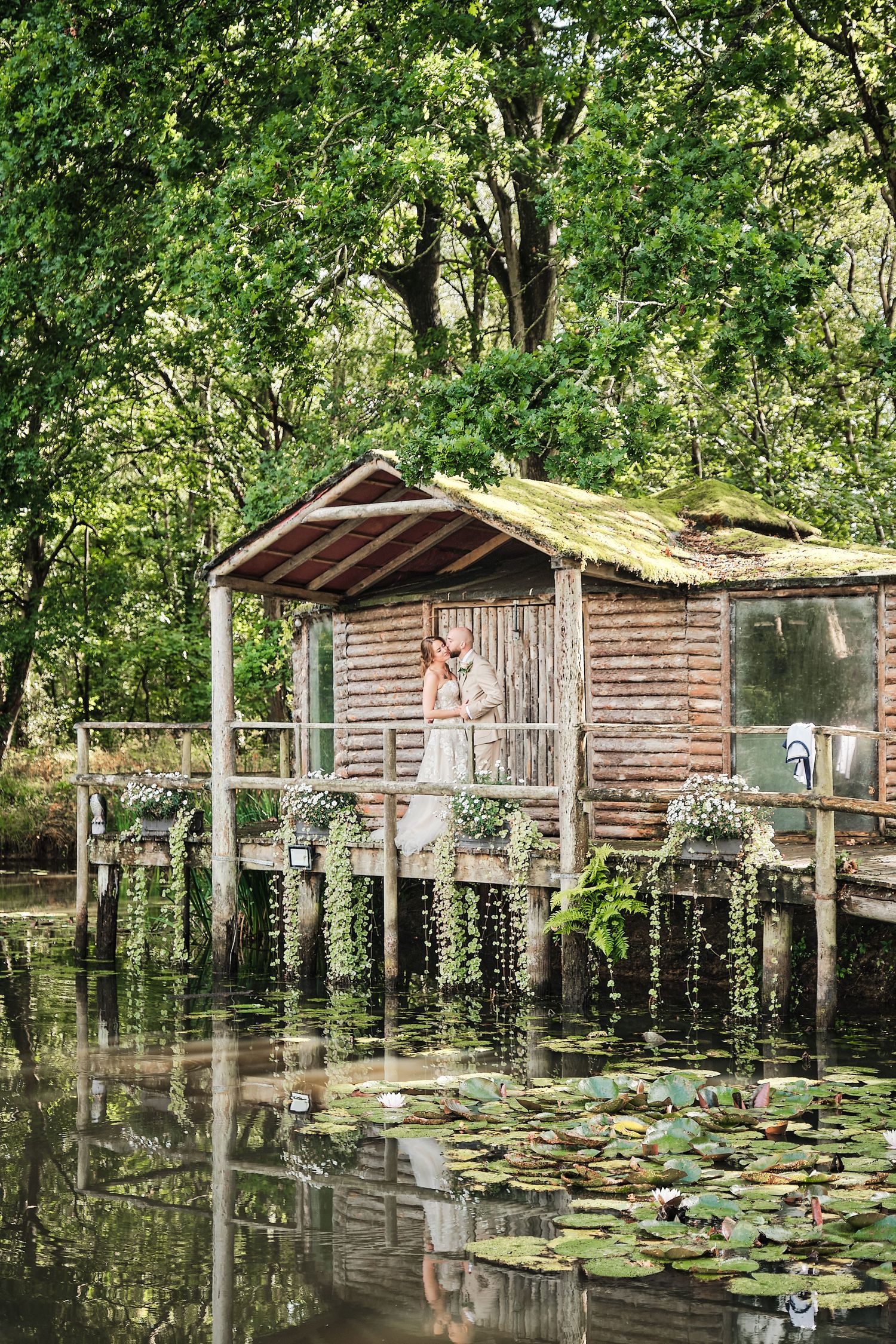 A rustic wooden fishing cabin on stilts over a tranquil pond Wedding Couple embrace by Jason Leaman Photography Surrey