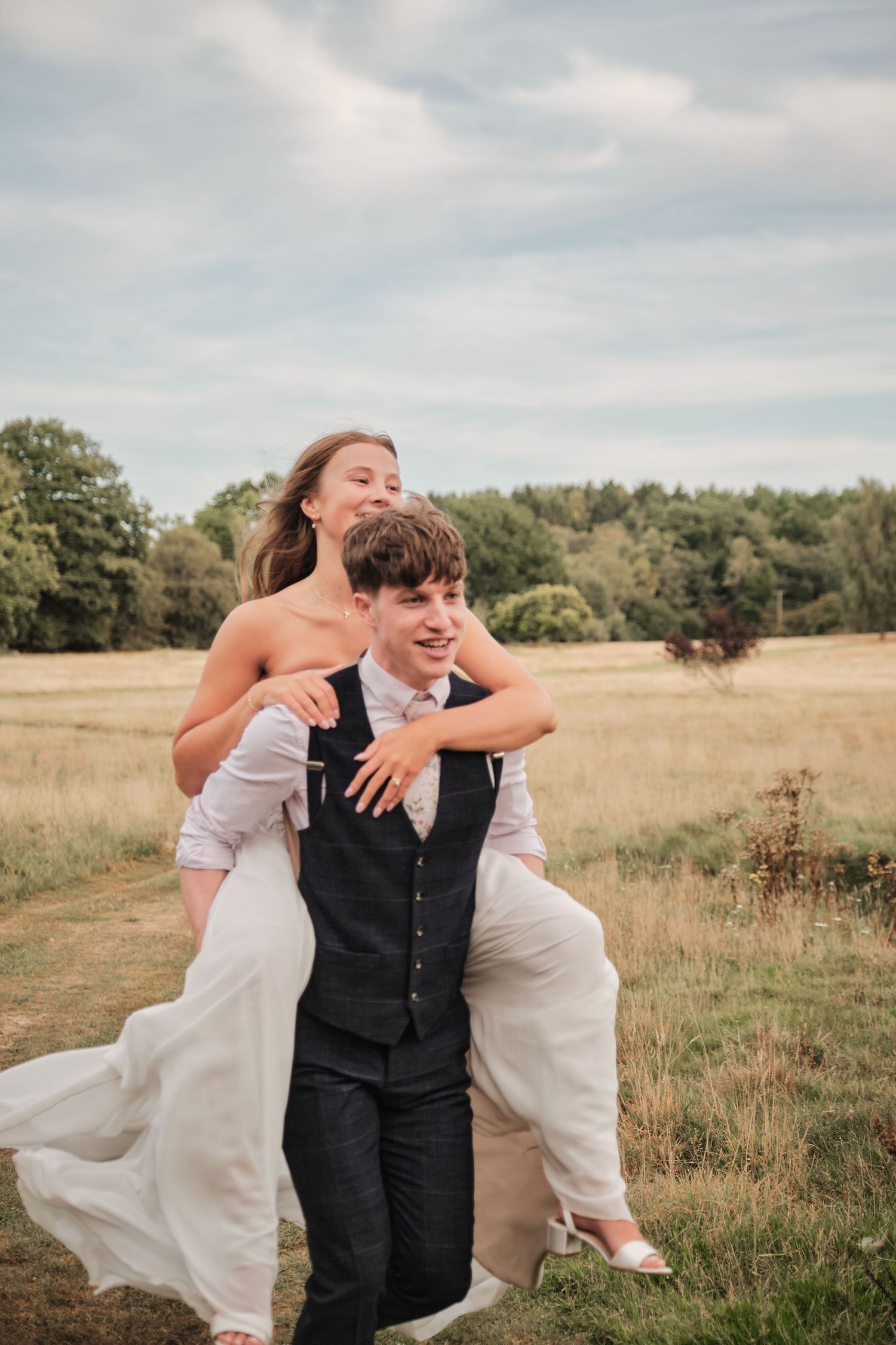 A couple embraces in a sunlit meadow wearing wedding attire on their special day.