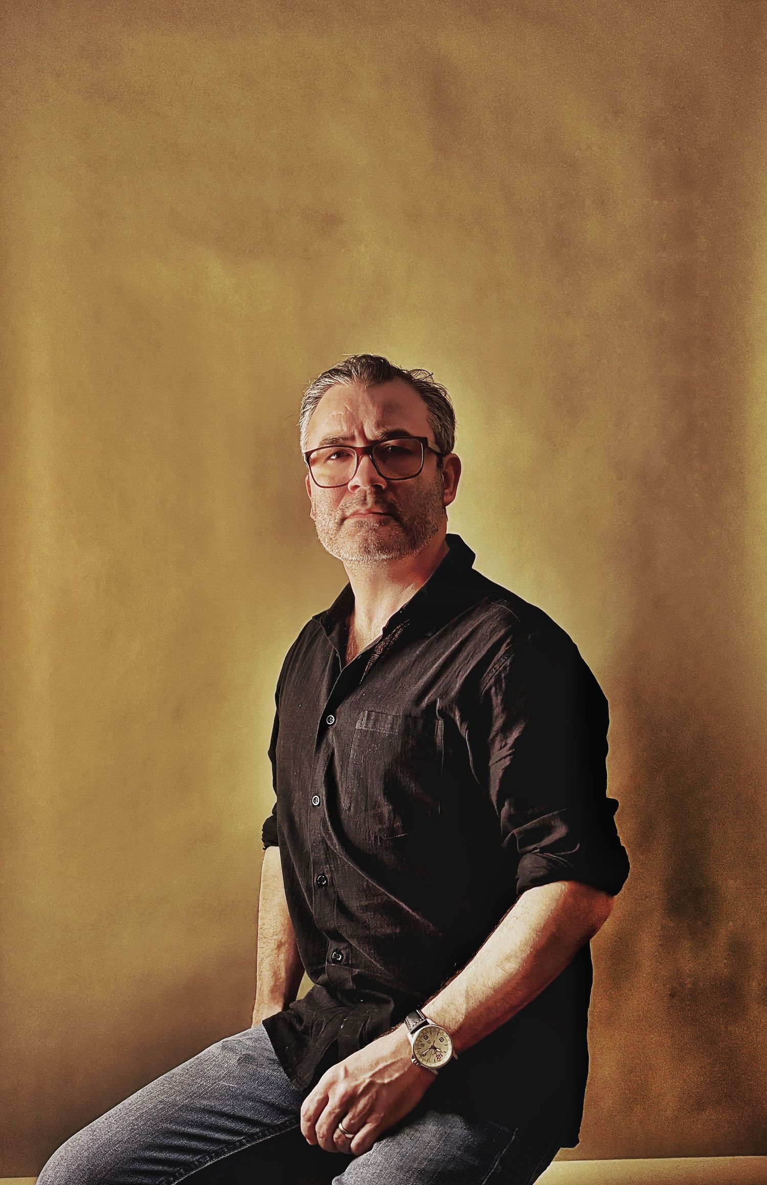A person in a black shirt sits casually against a textured brown wall in a series of portrait poses.