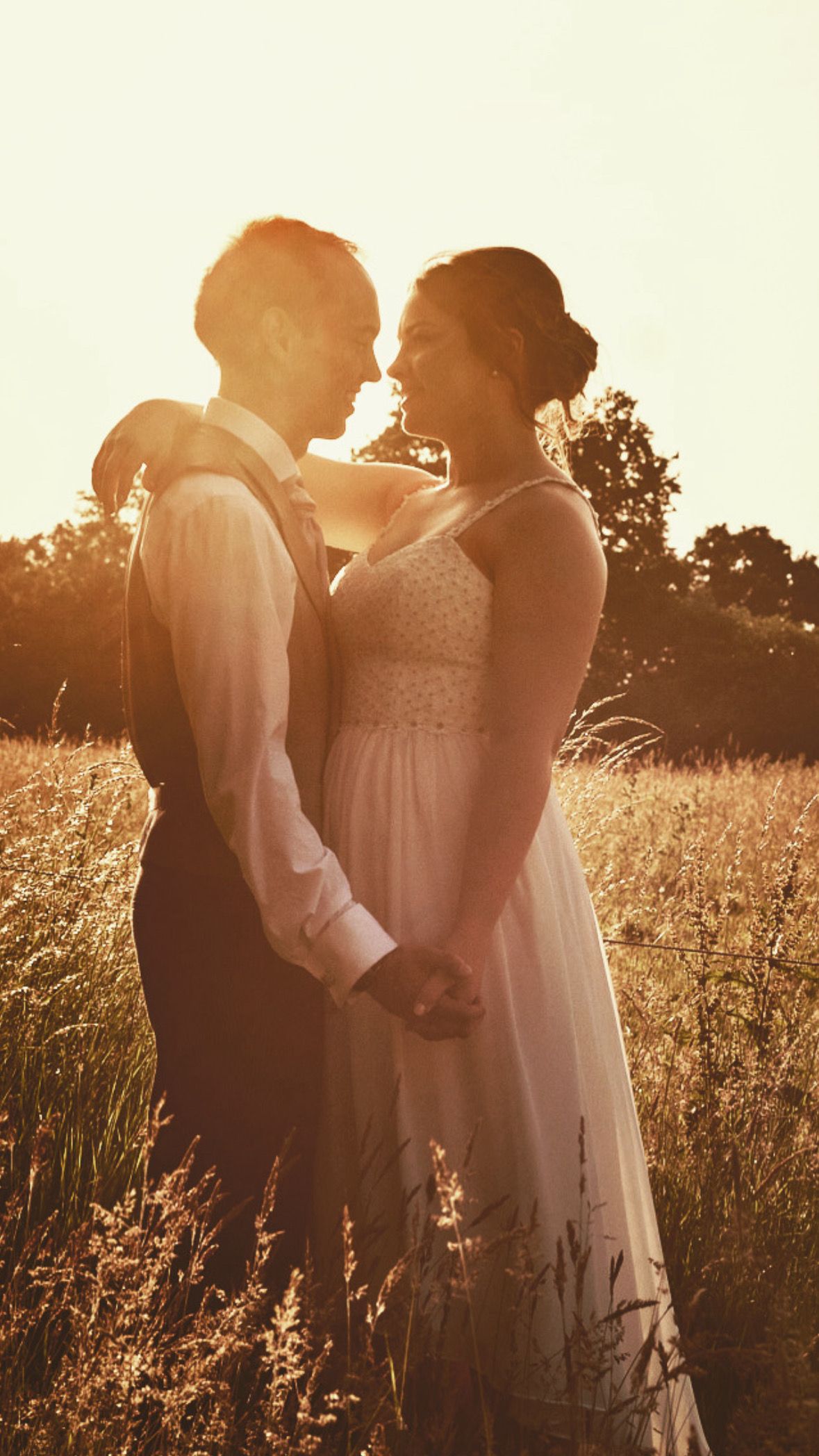 A romantic sunset wedding photo of a couple embracing in a golden field with warm backlighting.