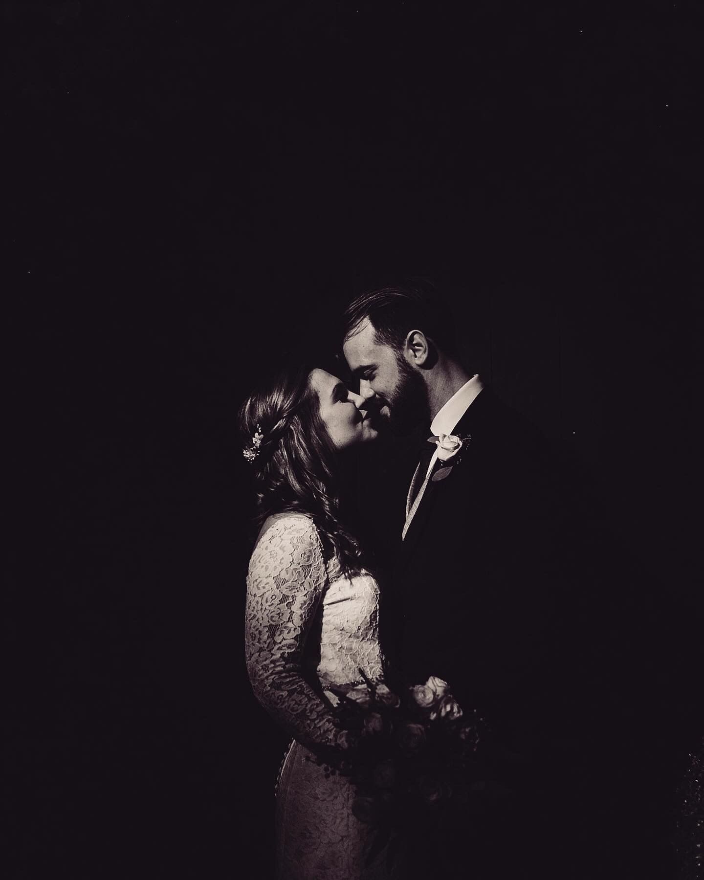 A romantic couple shares an intimate moment in dramatic low-key lighting creating a moody black and white portrait.