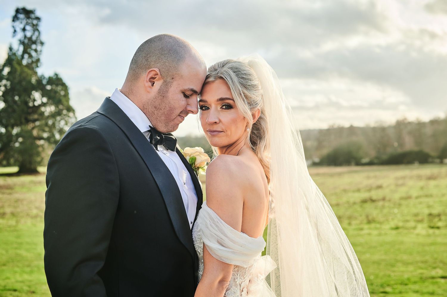 A romantic outdoor wedding photo series showing a couple in formal attire embracing in a sunlit field.
