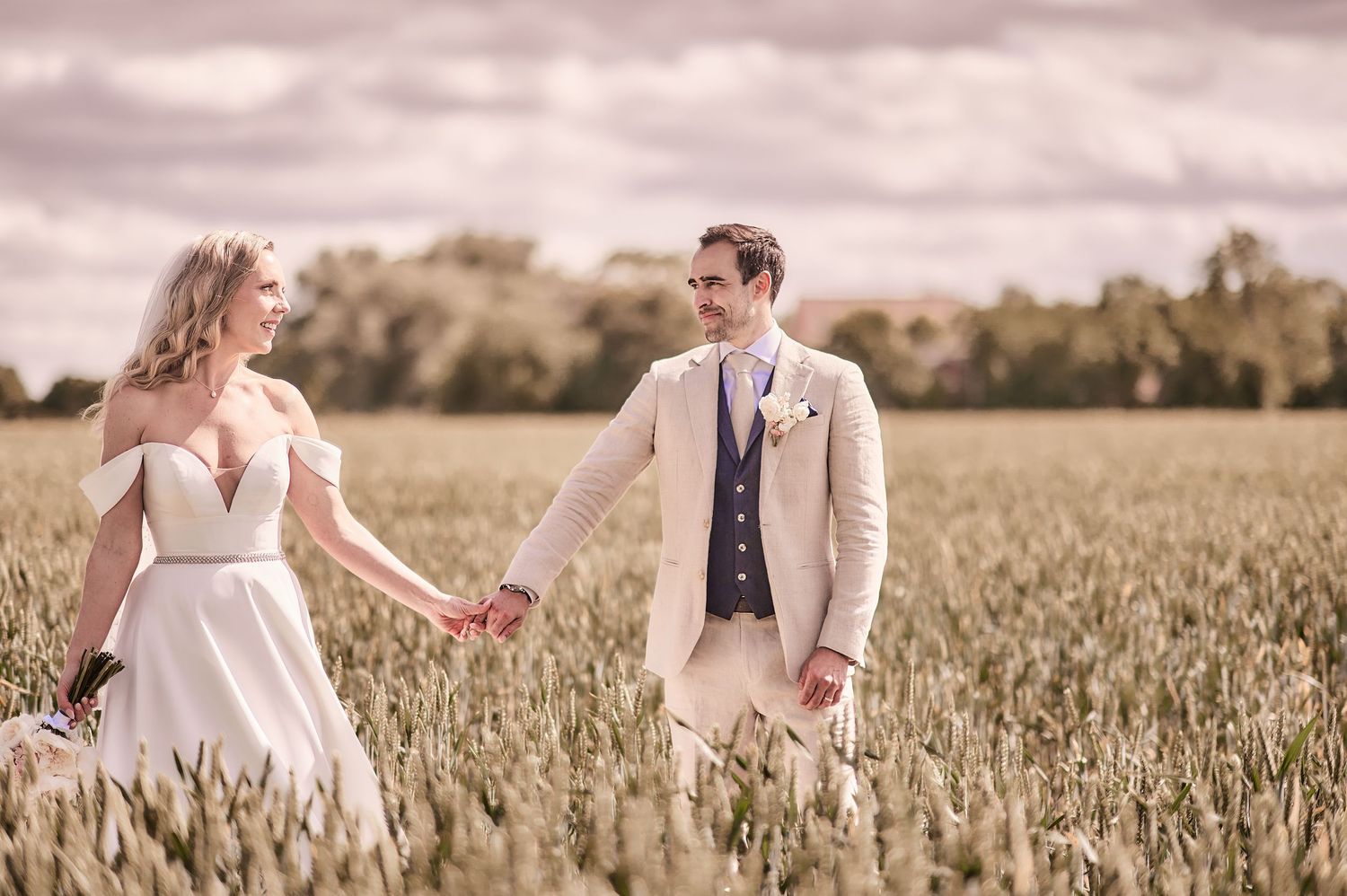 A bride and groom hold hands walking through a golden field on their wedding day.