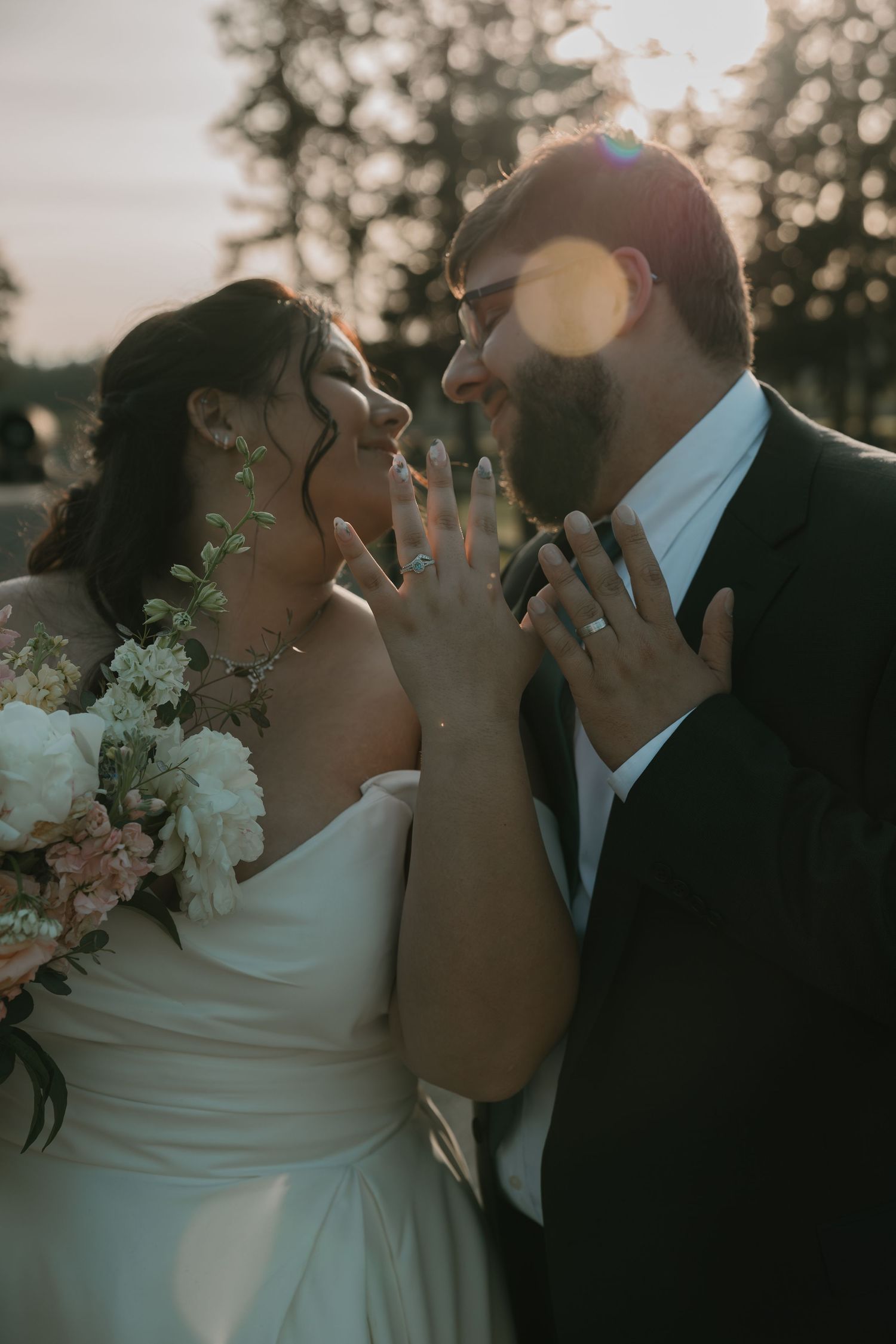 Romantic wedding couple shares intimate moments at sunset with bokeh lights and white floral bouquet in the background.
