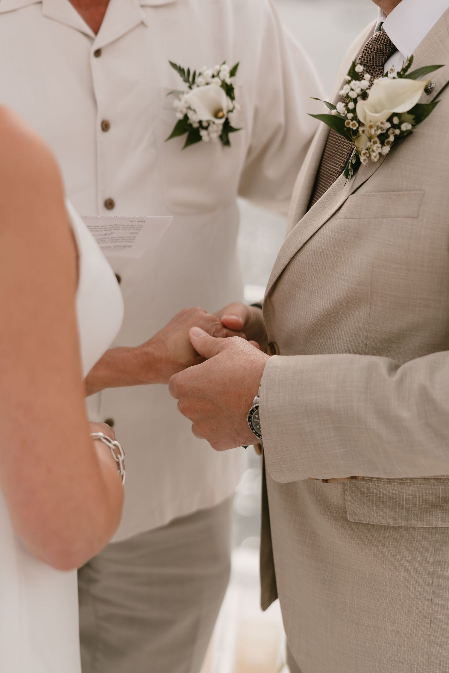 Close-up view of couple exchanging rings during wedding ceremony with white floral boutonniere detail.
