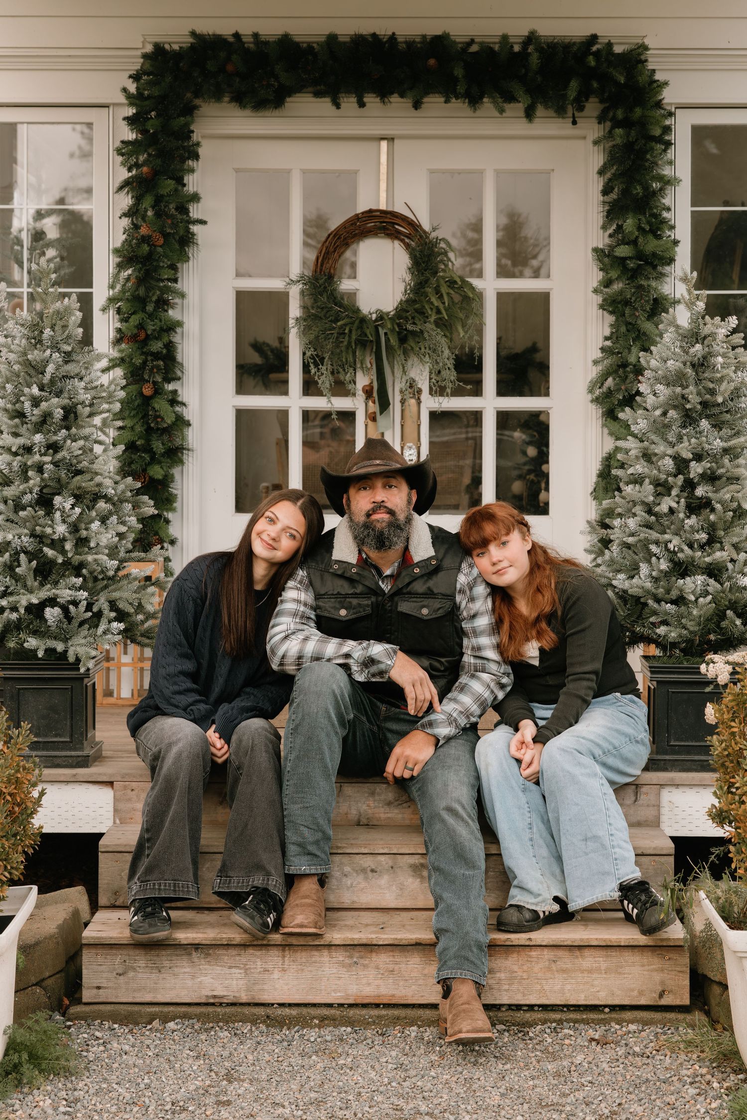 A cozy winter scene on a porch with evergreen decorations, a wreath on the door, and snowy flocked Christmas trees.