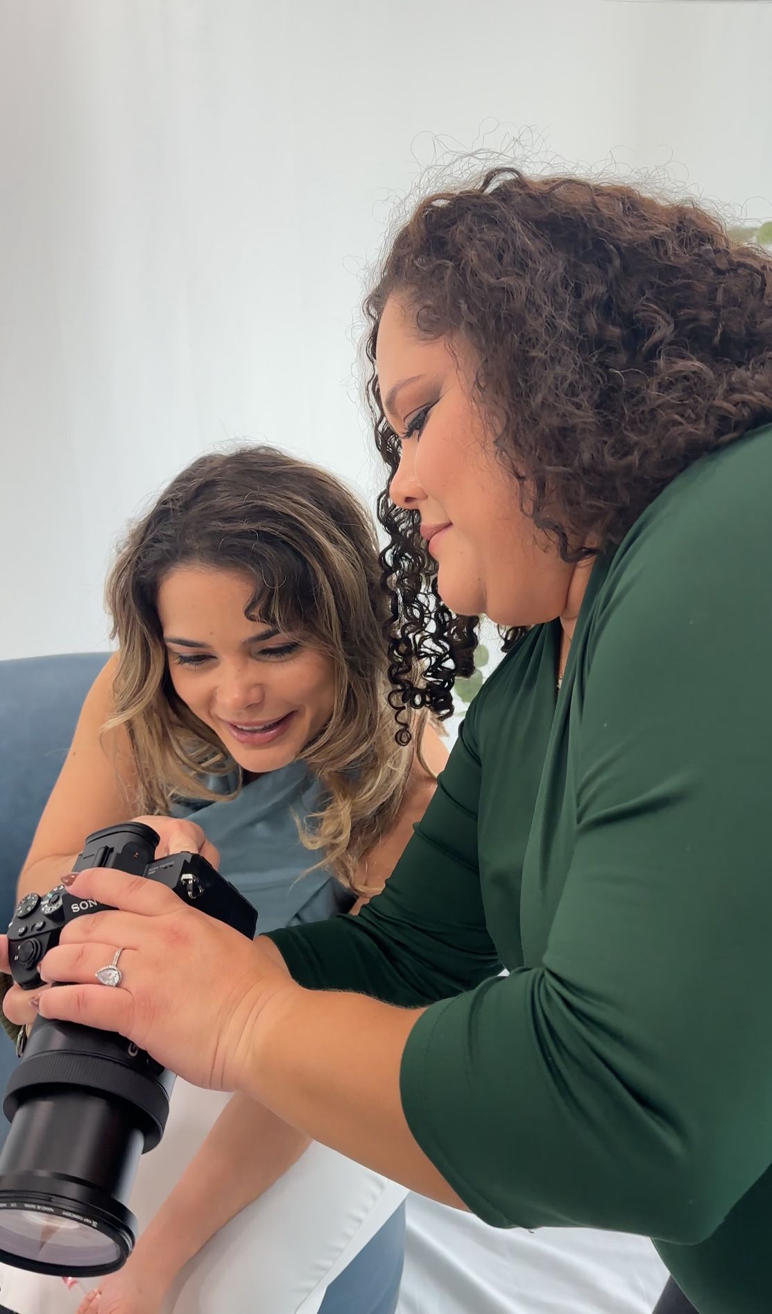Two photographers reviewing photos on a camera while sitting together on a blue couch.
