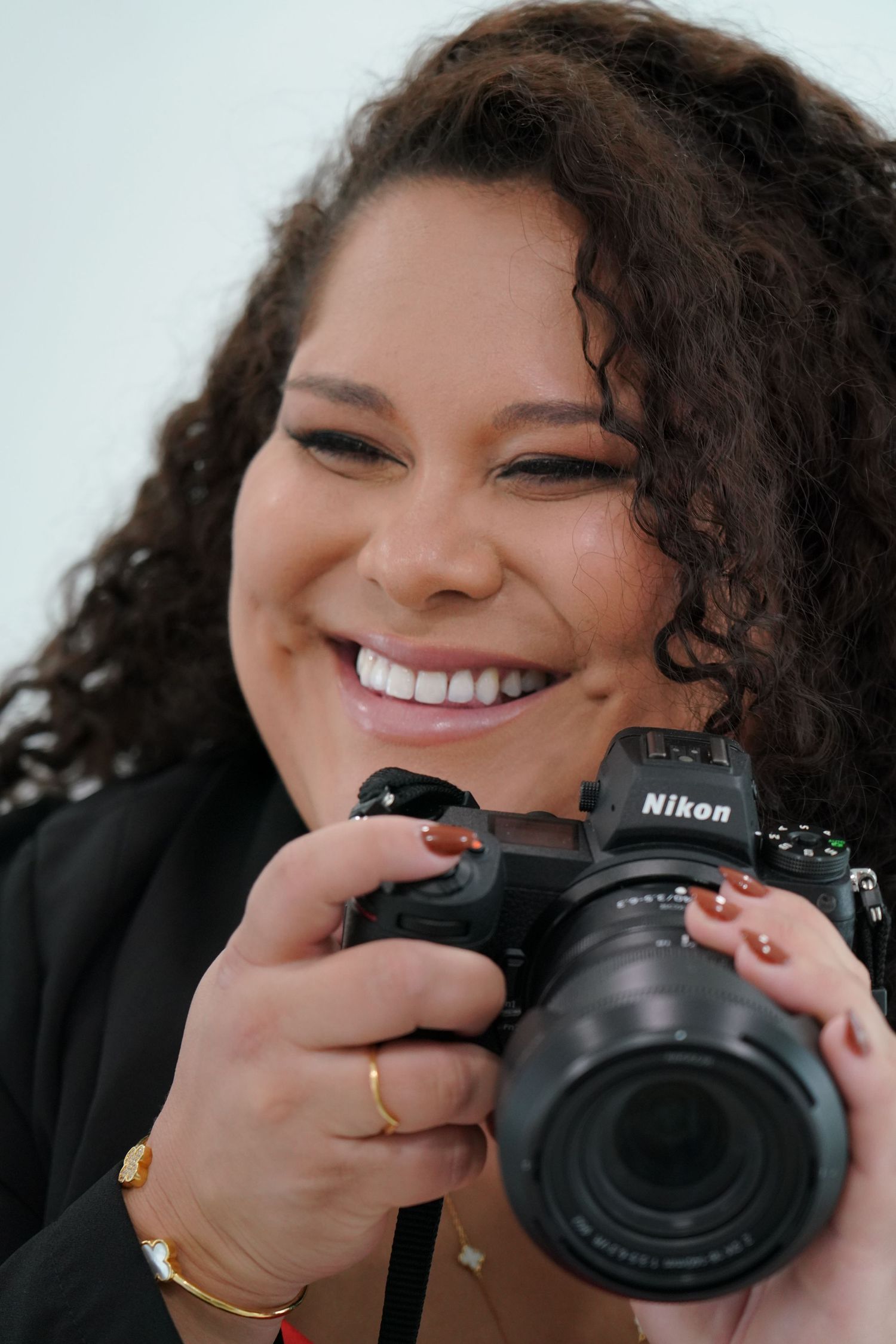 A photographer smiles while holding a professional Nikon camera with a telephoto lens.