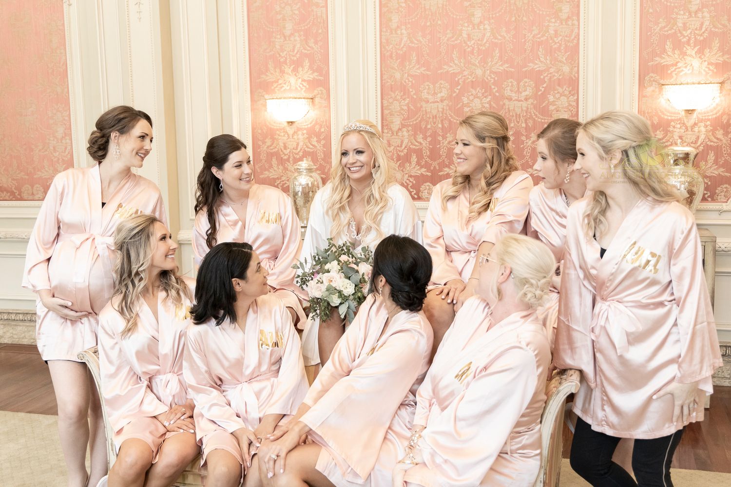 A group wearing matching pink satin robes poses together in a bridal party setting.
