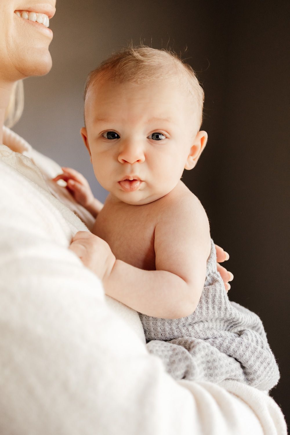 A baby looks directly into the camera while being held by his mom at his in-home newborn photoshoot