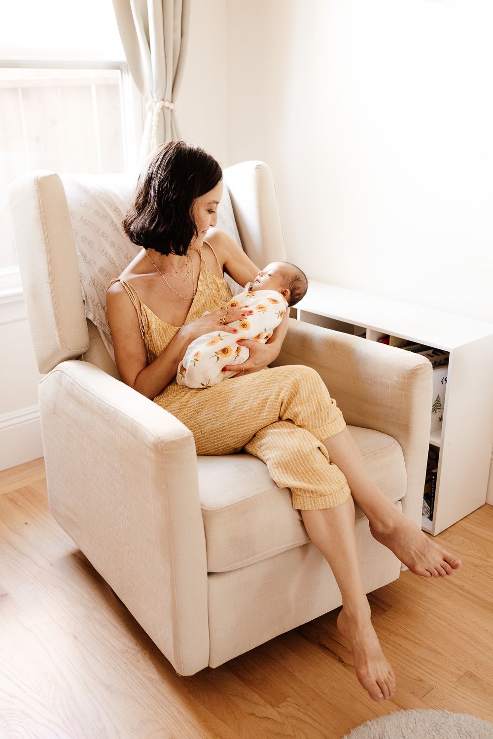 Mom cradles baby in chair by window at her in-home San Jose newborn session