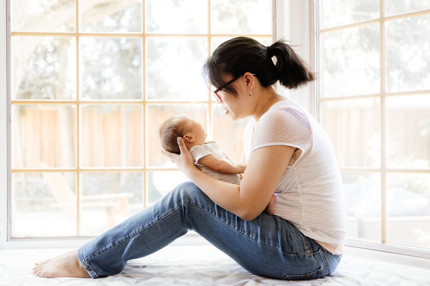A mom holds her newborn baby in front of a bay window in San Jose during her Bay Area newborn photography session