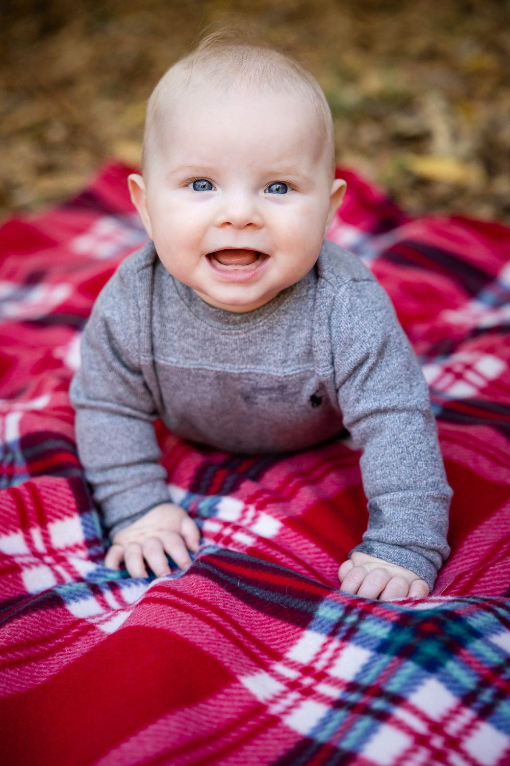 A young baby smiles at the camera on a plaid blanket