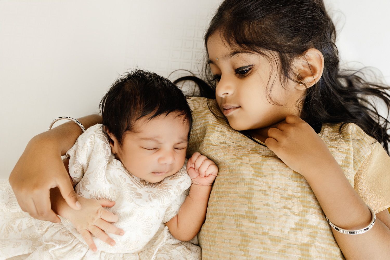 Sibling sisters snuggle on the floor at their in-home newborn photo session in San Jose