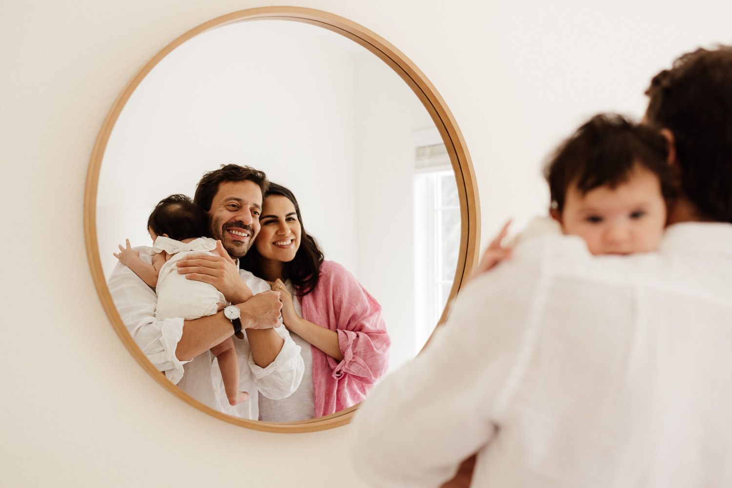 A family's reflection in a round mirror from their in-home newborn photo session