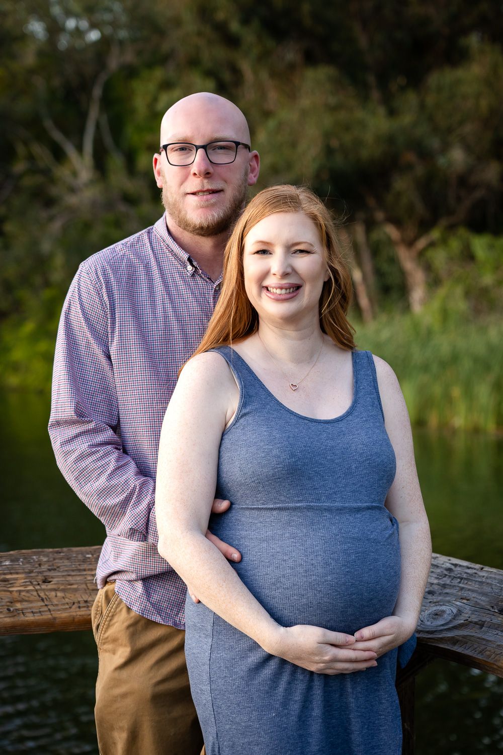 A Bay Area couple poses together outdoors, with the woman wearing a blue dress and the man in a purple shirt against a natural backdrop.
