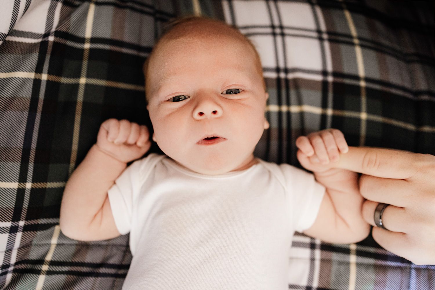 A baby looks directly into the camera on a plaid blanket