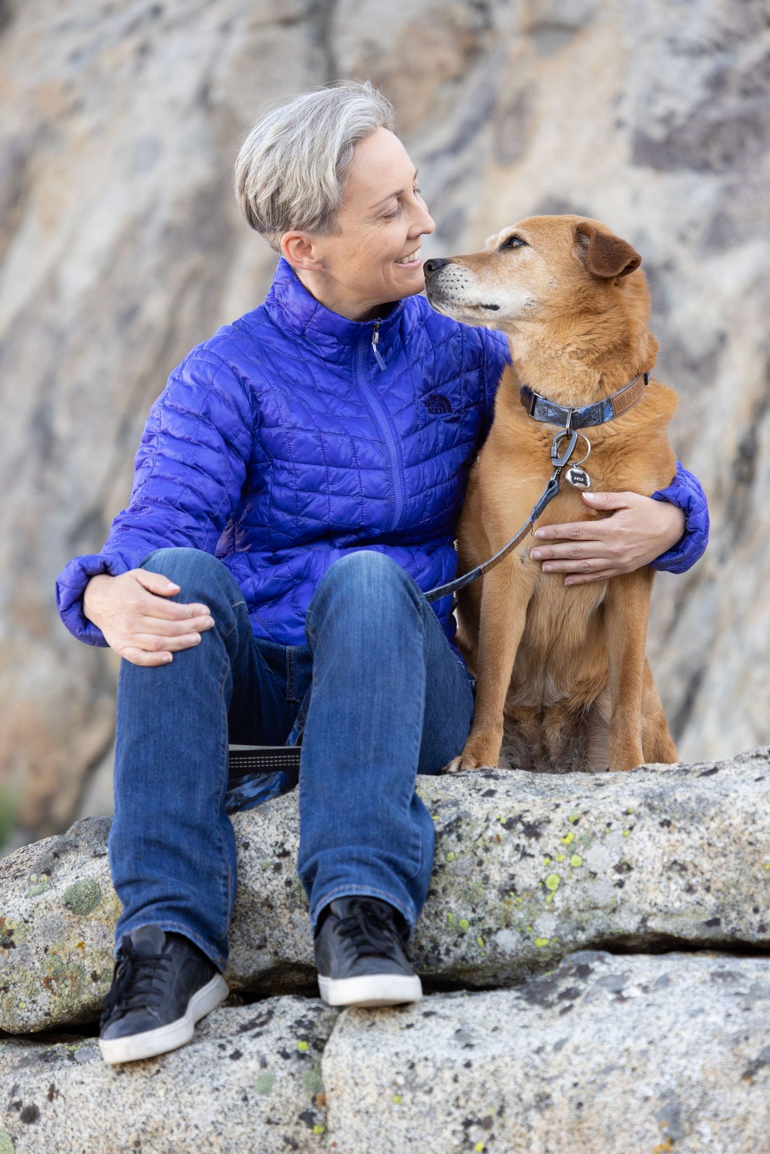 Woman lovingly looks at her dog while sitting on rocks in Truckee