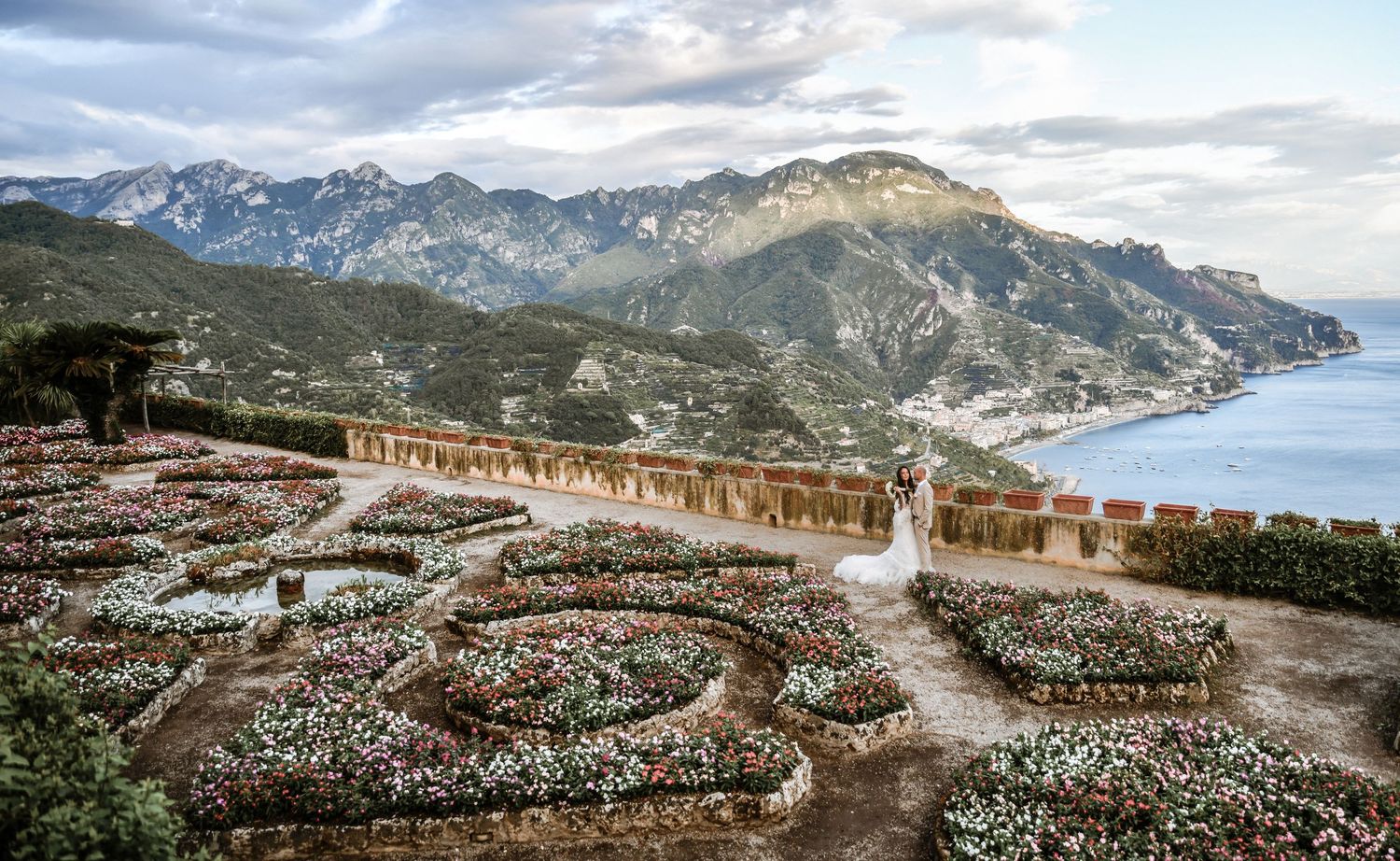 Panoramic mountain vista with winding pathways and stone structures overlooking a dramatic coastal landscape at sunset.