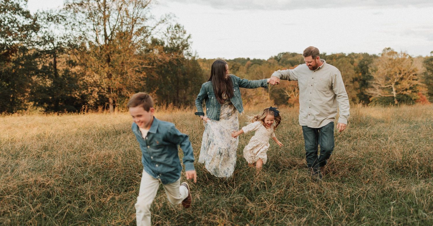 People run and play together in a golden autumn field surrounded by trees at sunset.