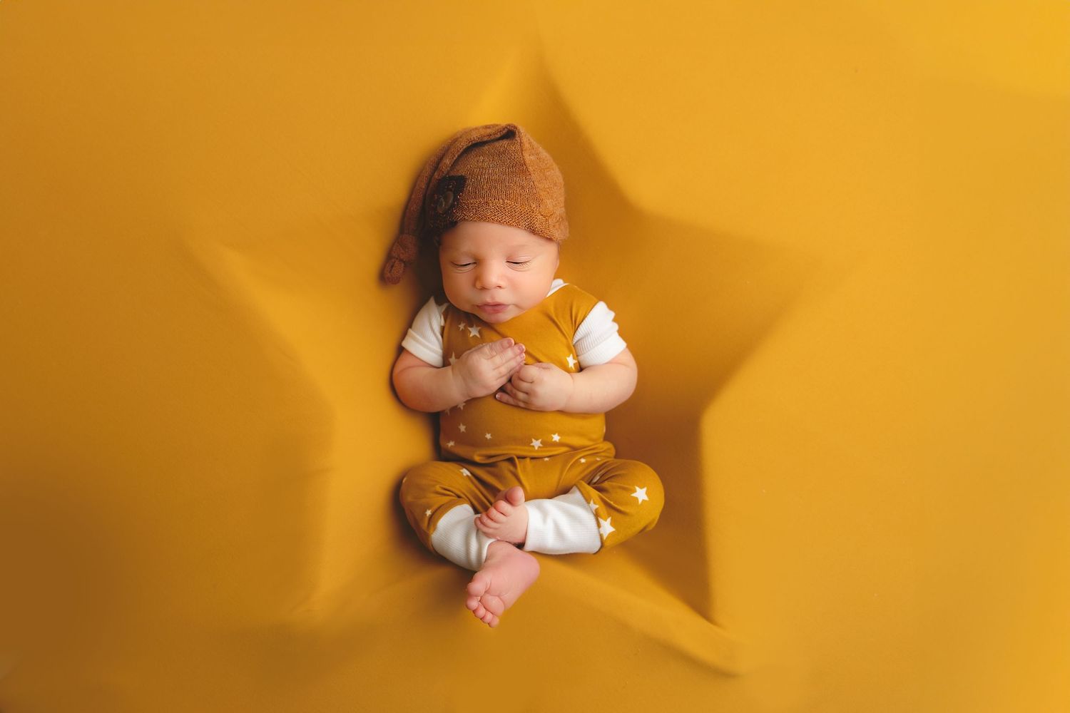 Baby posed in yellow star-shaped setting wearing neutral colored outfit.