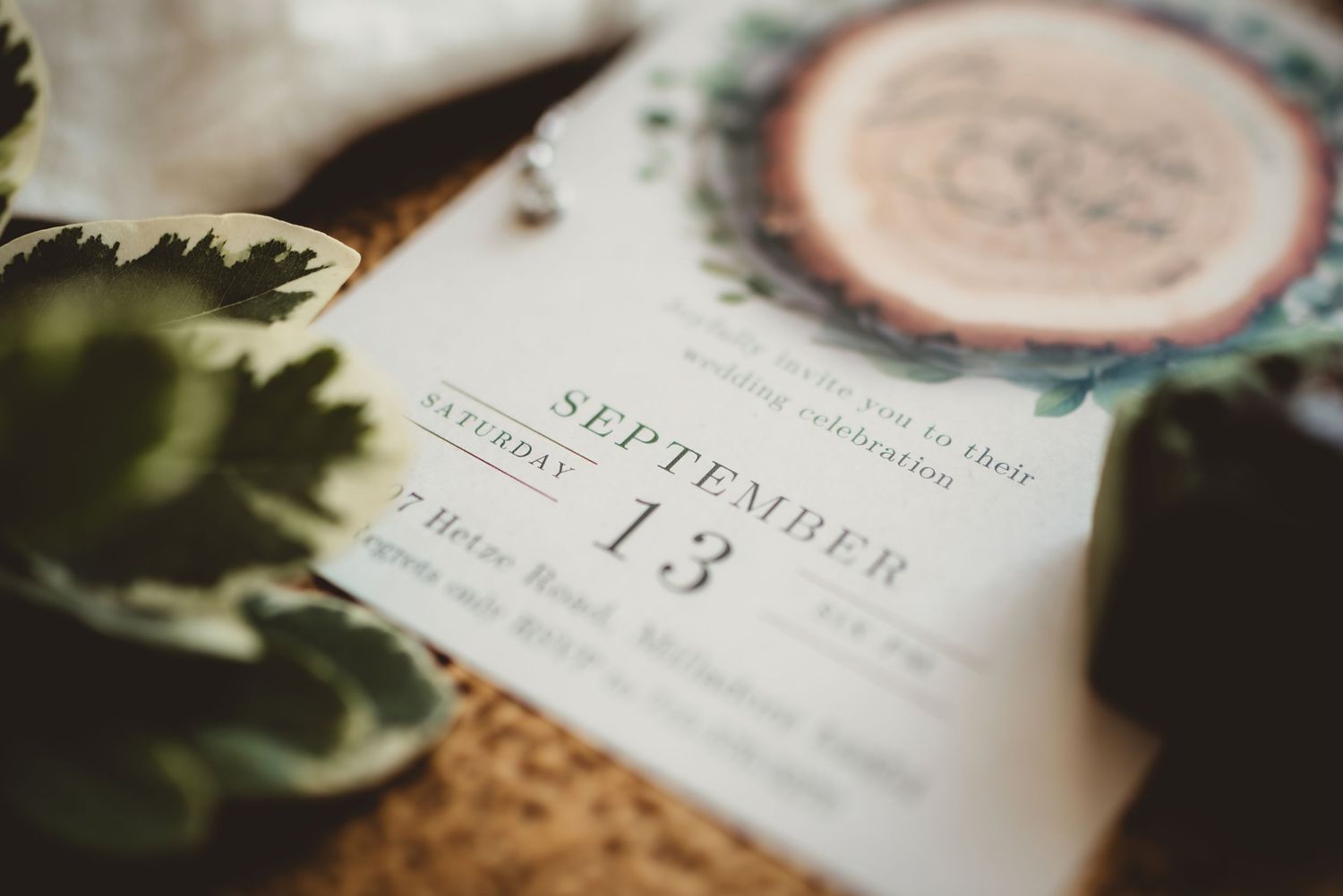 Close-up of a wedding invitation for Saturday, September 13, with floral details, surrounded by greenery.