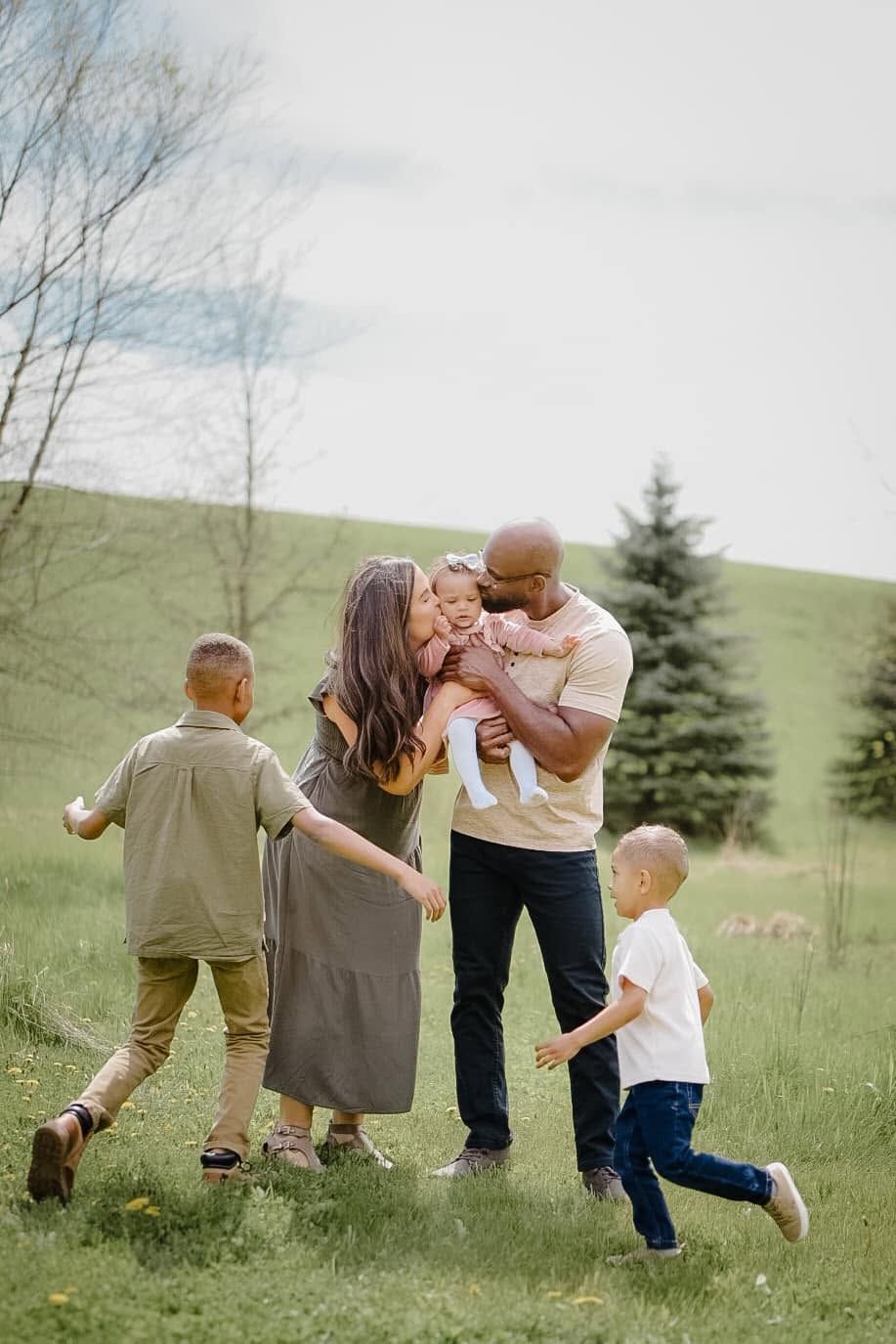 Joyful interracial family with three children playing outdoors on a lush green field during a spring family photo session.
