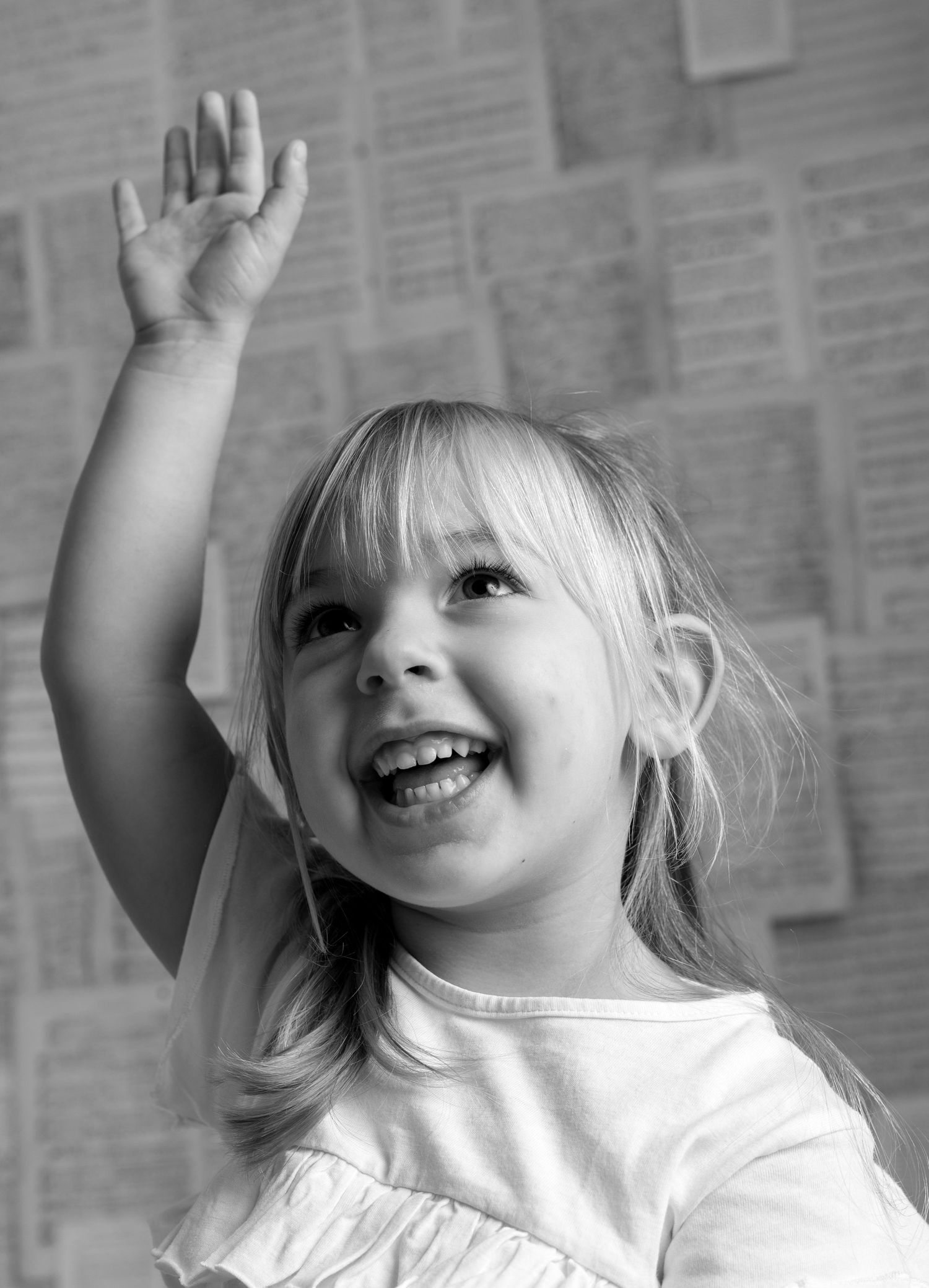 A joyful child raises their hand high in the air while smiling, captured in black and white photography.