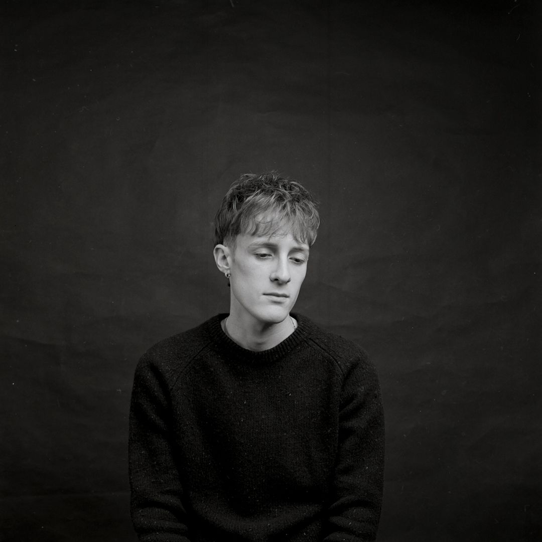 Black and white portrait of a person in a dark sweater with eyes closed against a dark background.