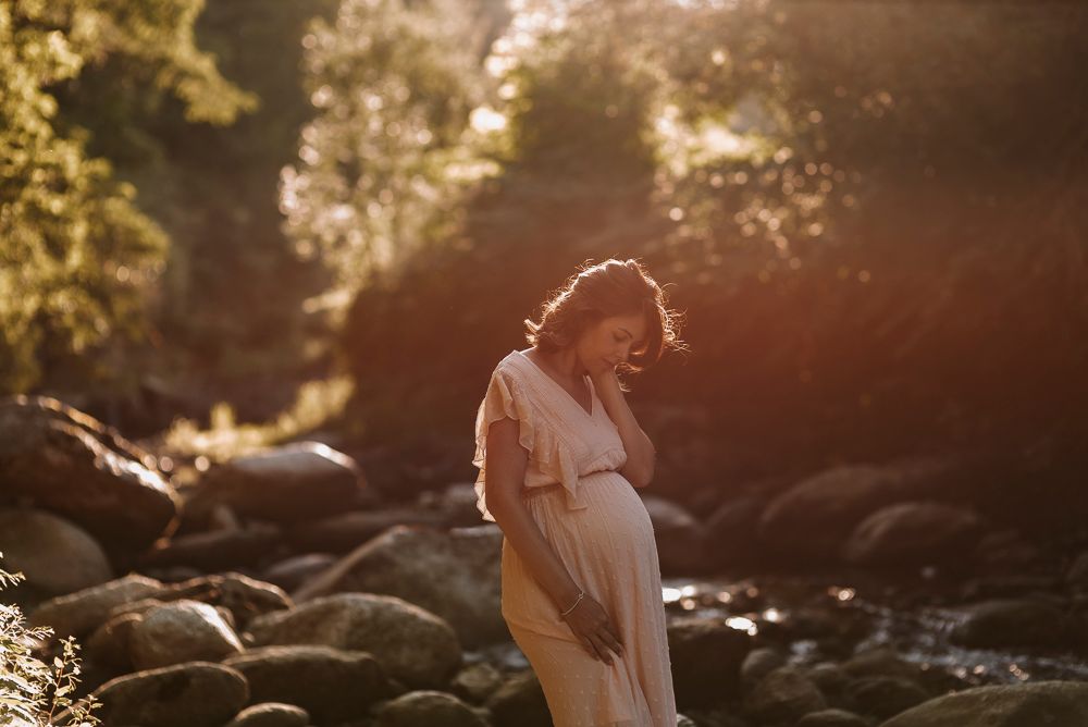 Silhouetted couple embraces in golden sunlight among rocks and trees during sunset photography session.