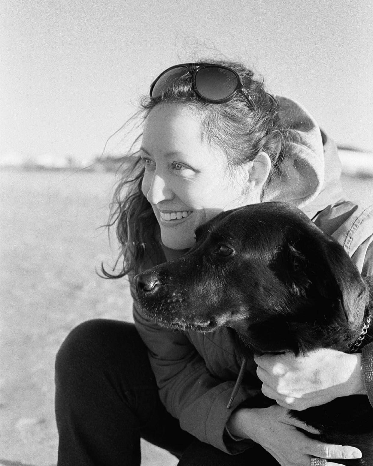 A person and a black dog share an affectionate moment in a series of black and white photographs.