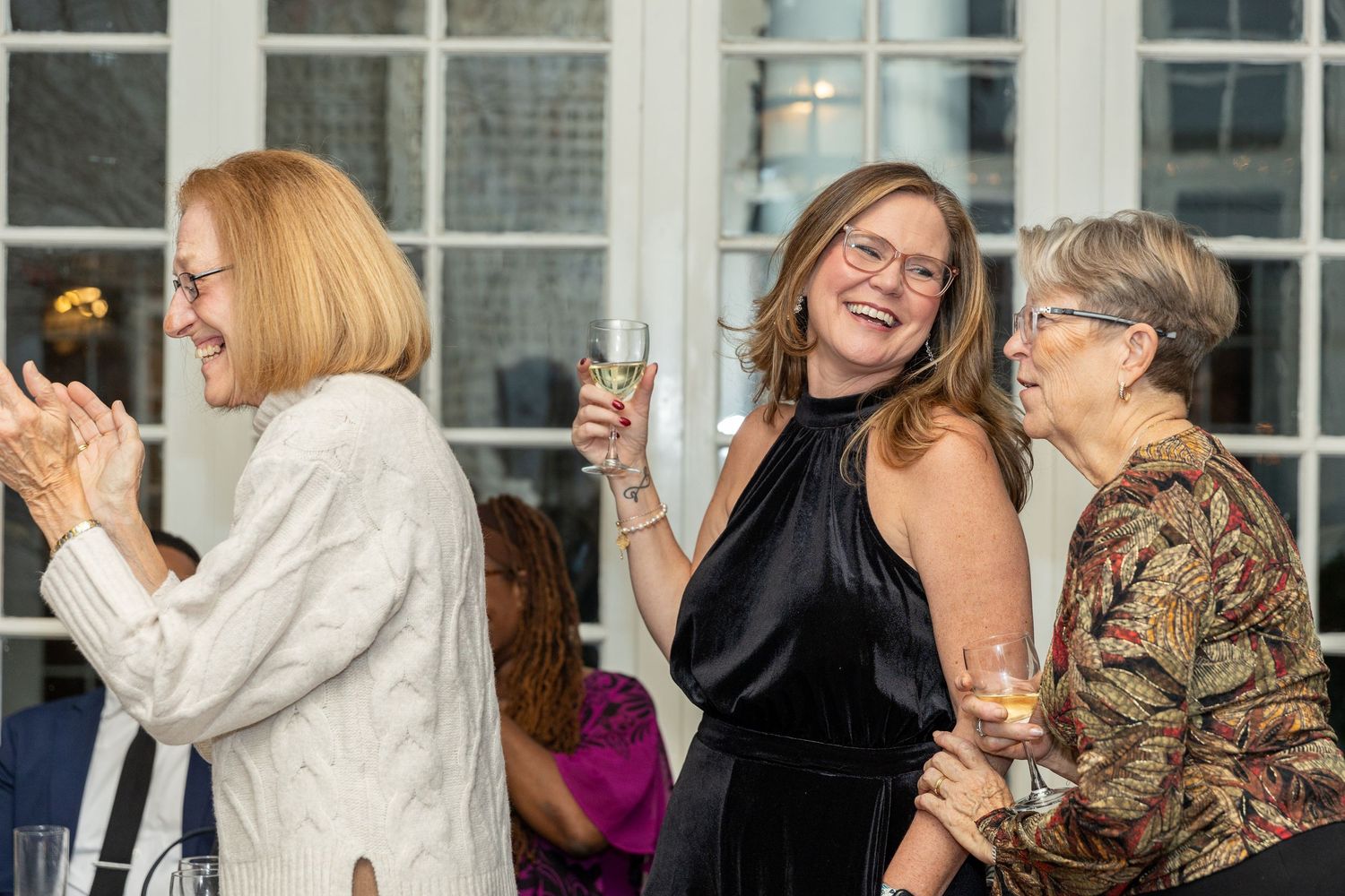 Three women laughing and celebrating together while holding drinks at an elegant party event.