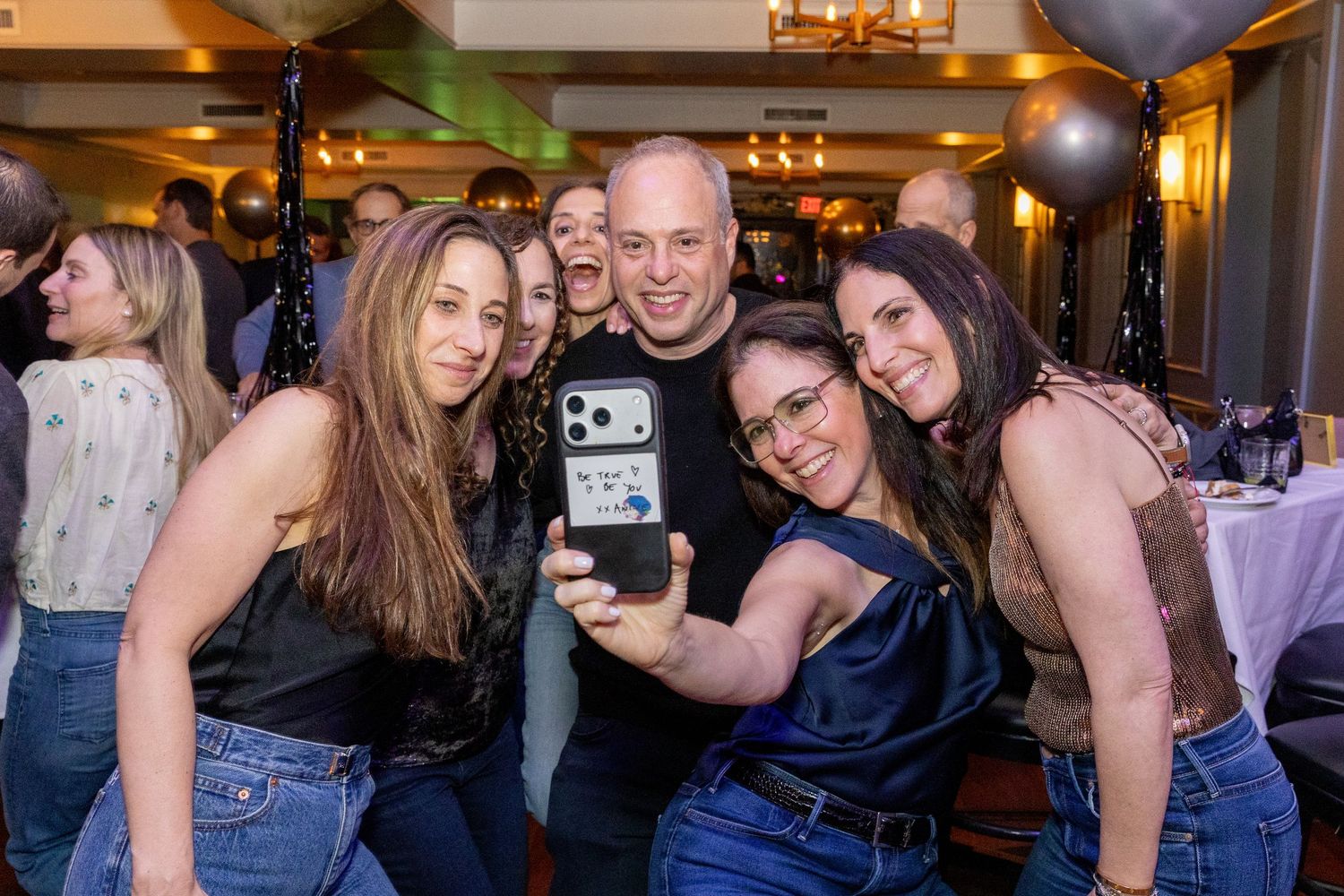Group of friends taking a fun selfie together at an indoor party with balloons and festive decorations.