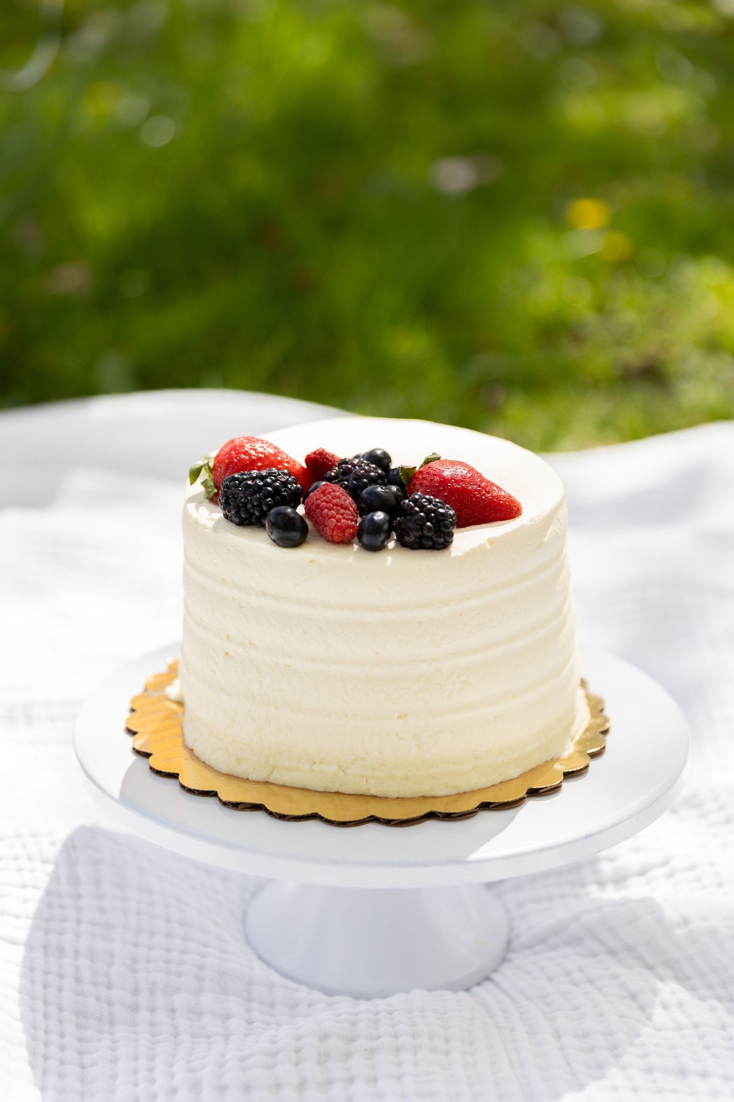 Elegant white birthday smash cake topped with fresh strawberries, blackberries, and blueberries on cake stand.
