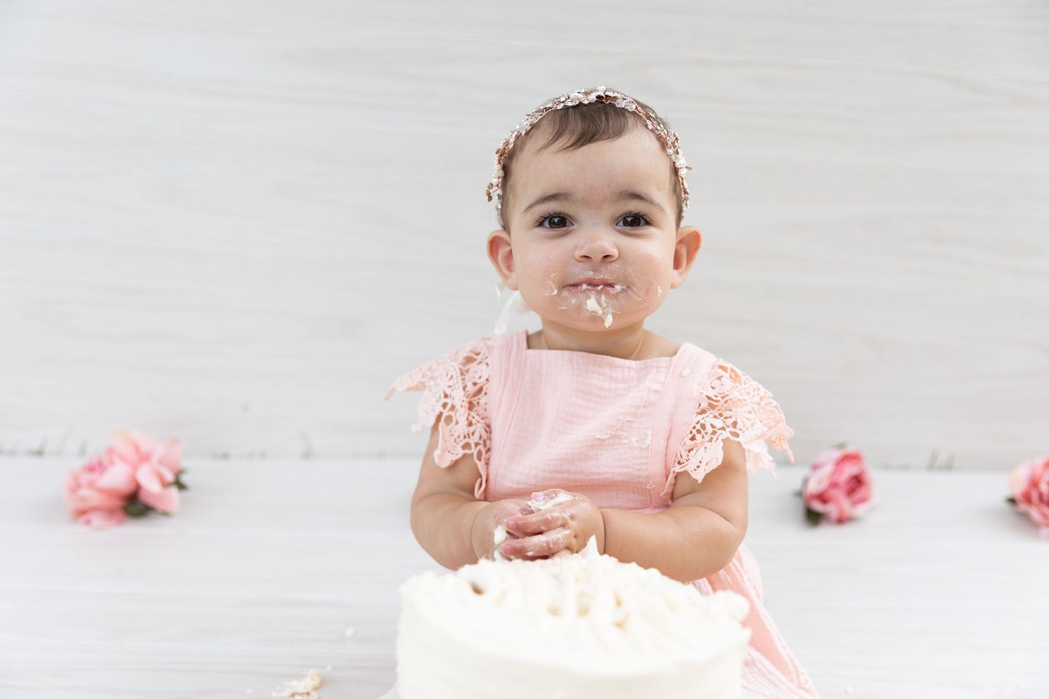 Adorable baby girl in pink dress with cake smeared face at first birthday smash session.