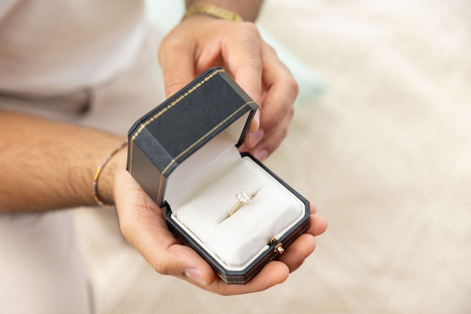 Close-up of elegant diamond engagement ring displayed in open jewelry box held by hands.