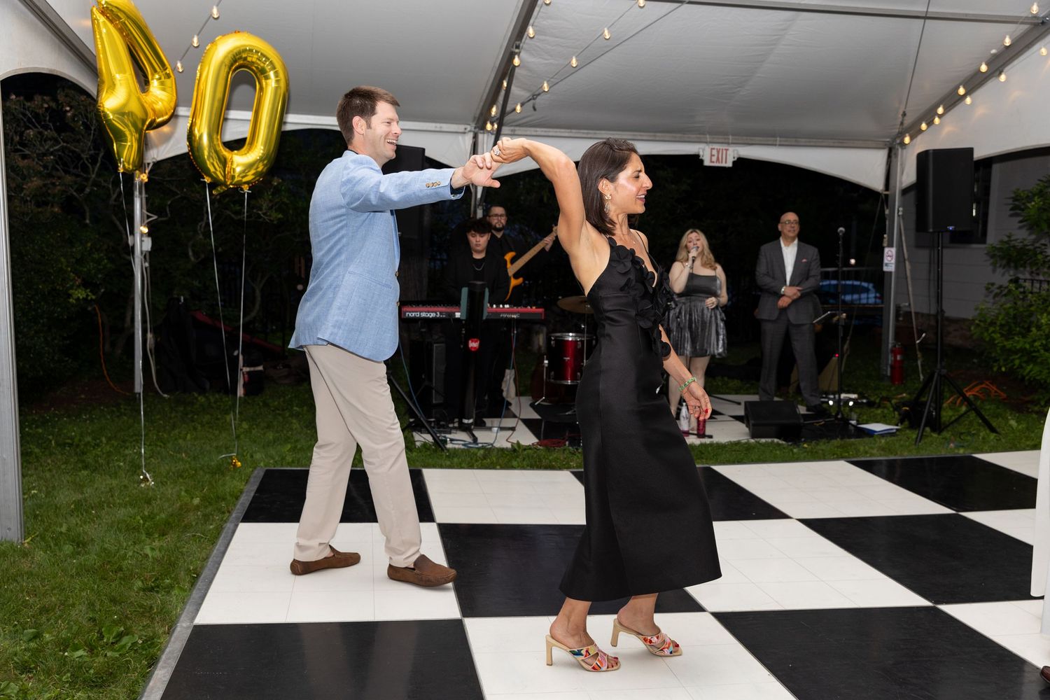 Couple dancing under a tent with gold 40 balloons at an outdoor birthday celebration.