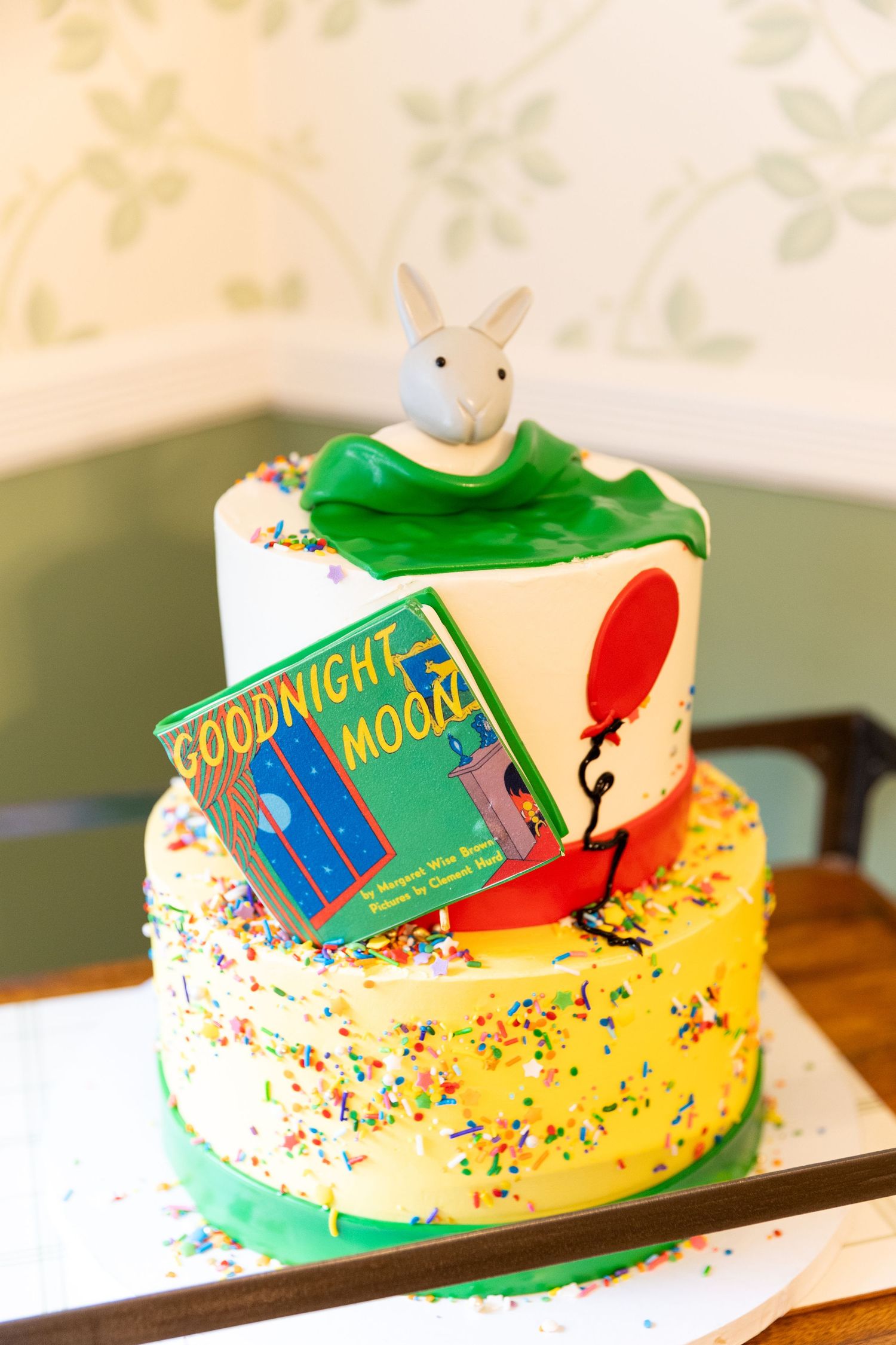 Three-tier birthday cake with Goodnight Moon book design, sprinkles, and bunny topper.