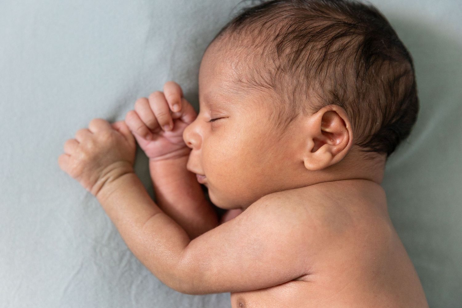 Peaceful newborn baby sleeping on a light blue blanket with hand raised near face.