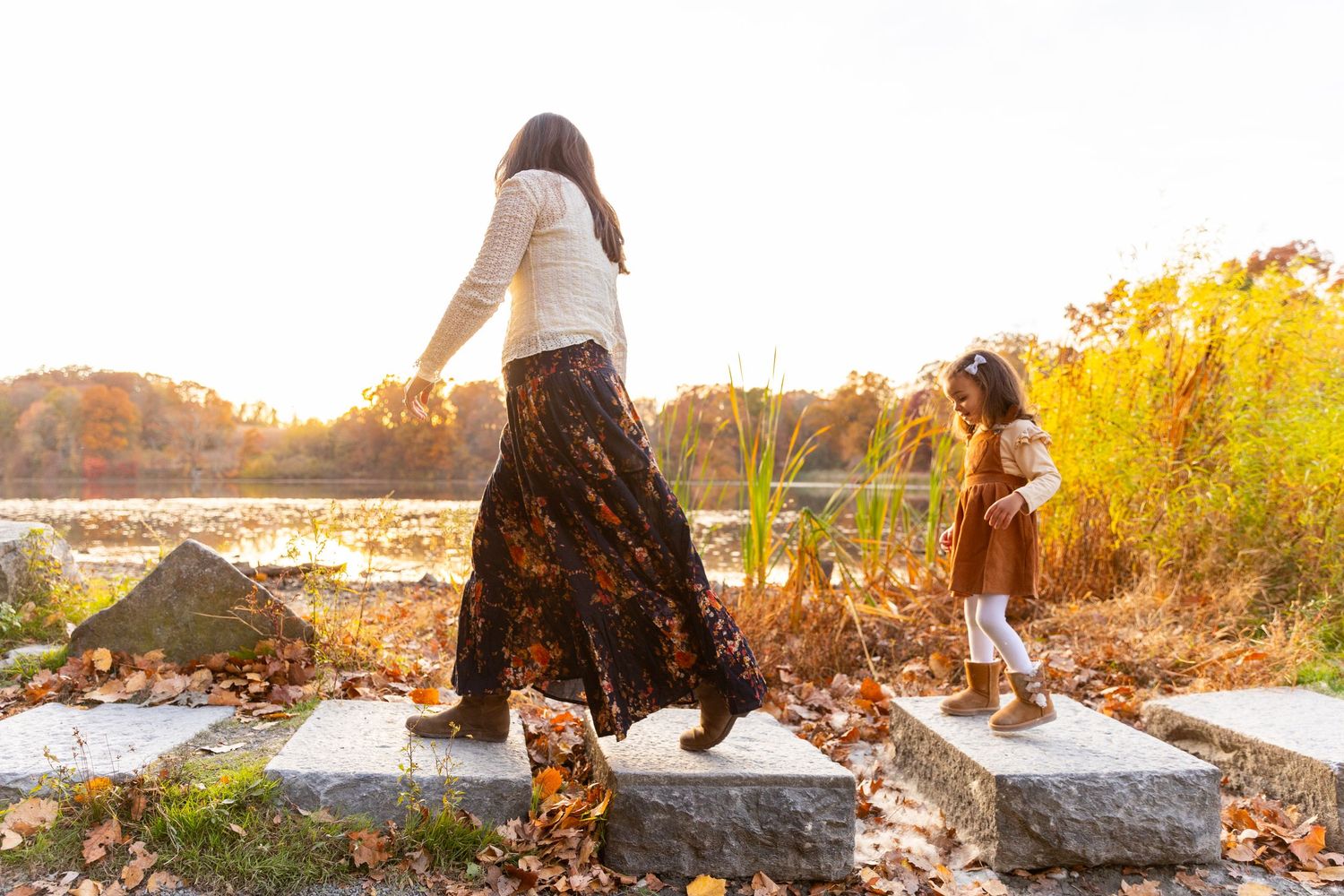 Mother and daughter walking on stone steps near a lake with golden fall trees.