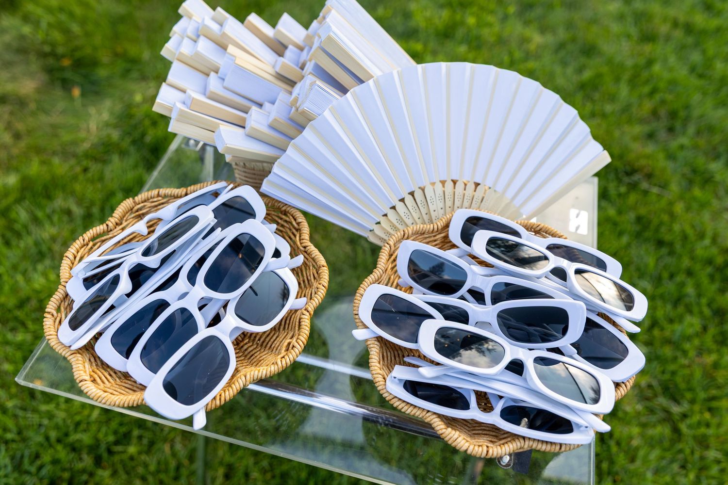 White hand fans and sunglasses party favors displayed in wicker baskets outside.