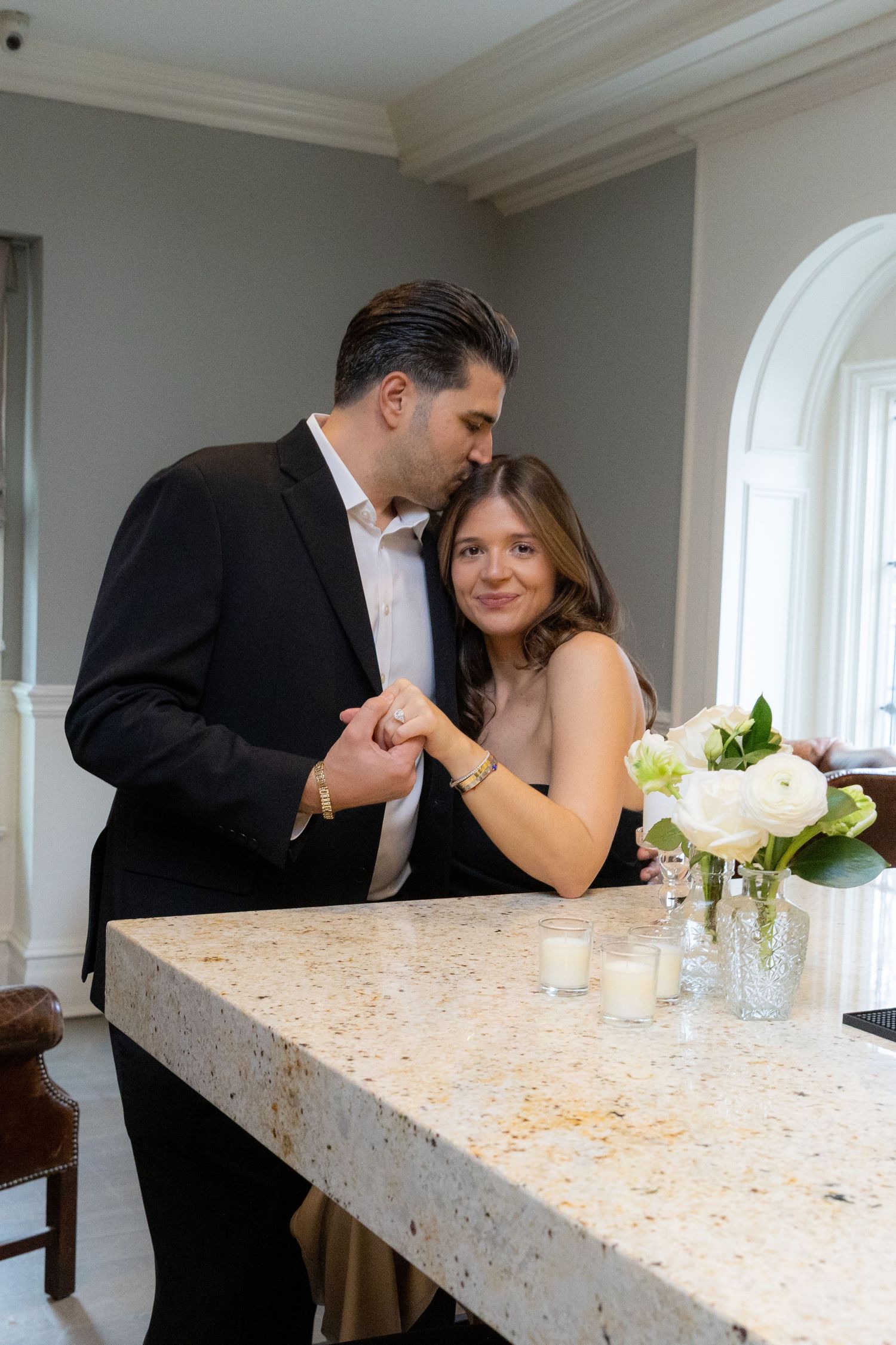 A couple shares a romantic moment holding hands at a marble countertop with white roses nearby.