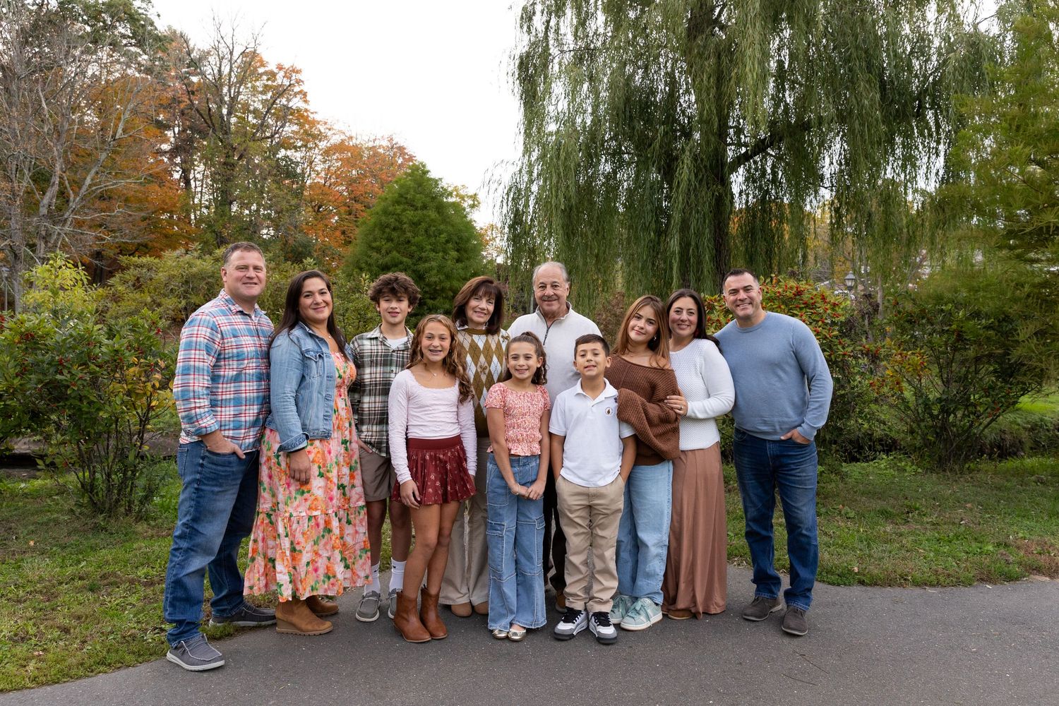 Extended family group of ten adults and children posing outdoors among fall foliage.