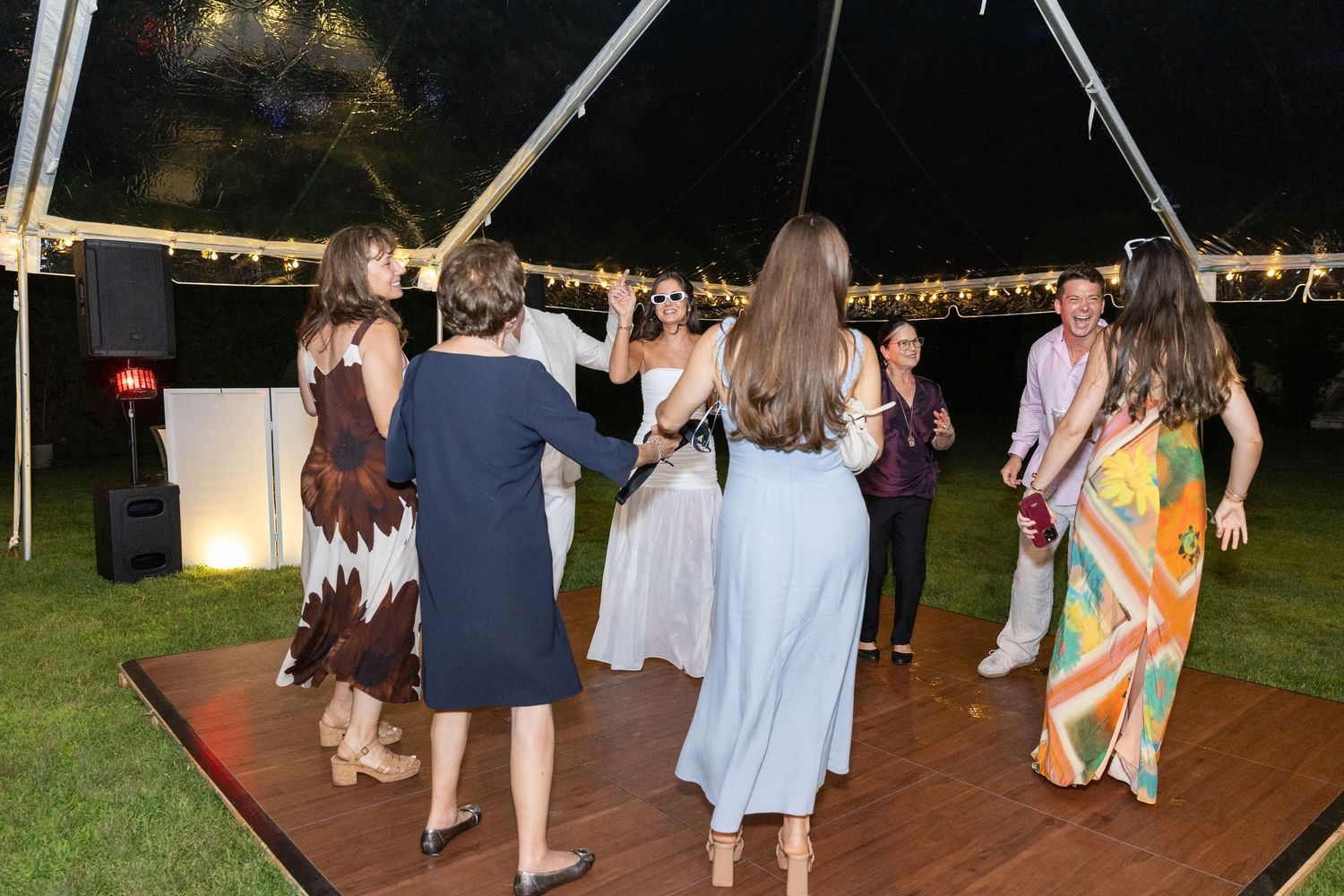 Guests dancing together under a white tent at an elegant outdoor evening wedding reception.
