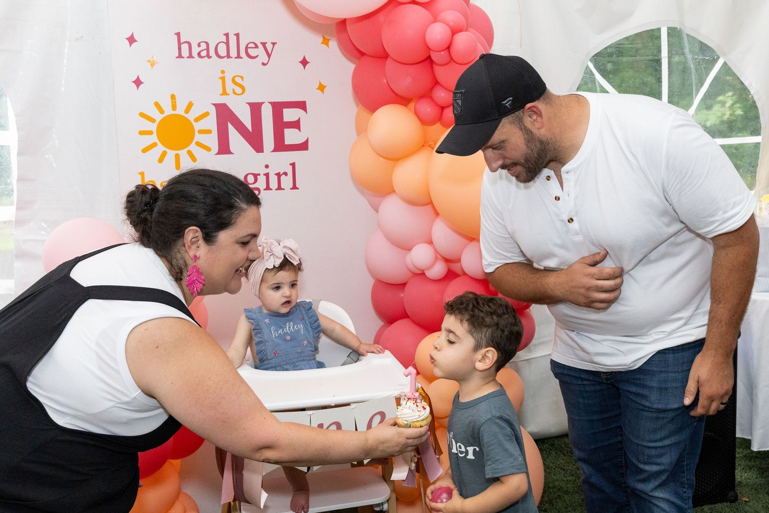 Family celebrating baby Hadley's first birthday with colorful balloon arch backdrop.